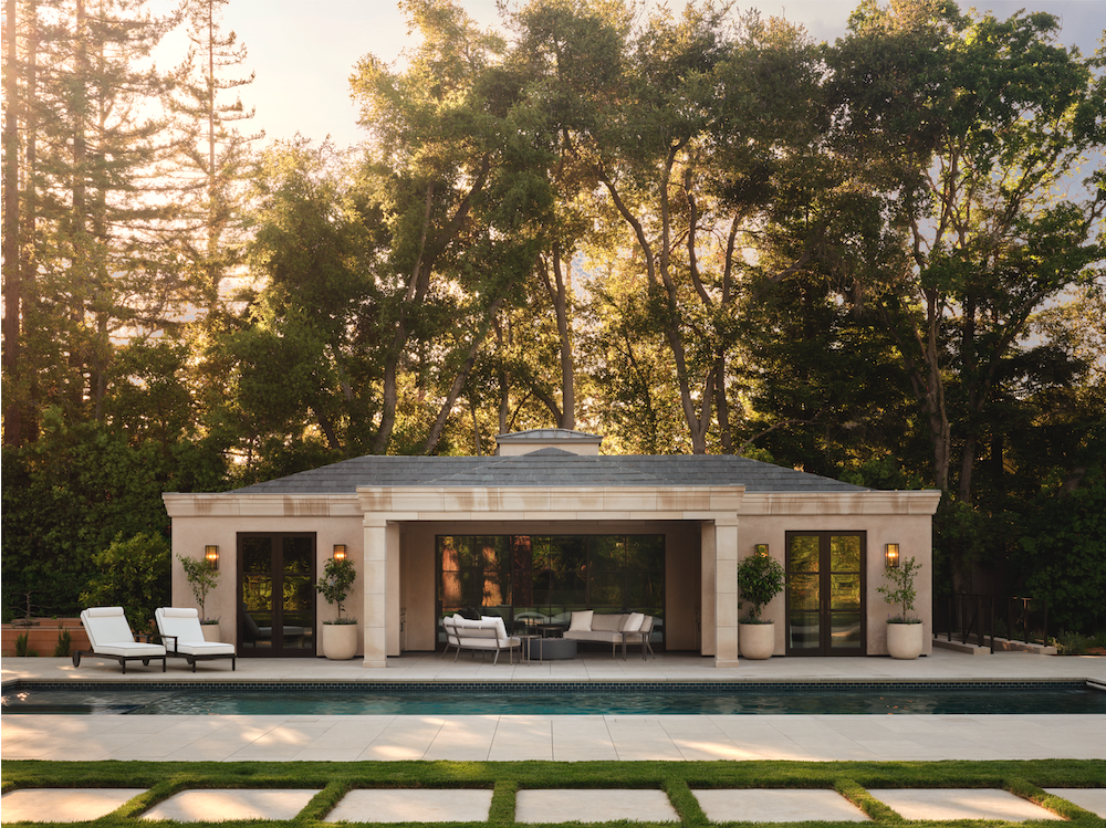 A modern backyard with a swimming pool, outdoor seating area, and a single-story house surrounded by trees.