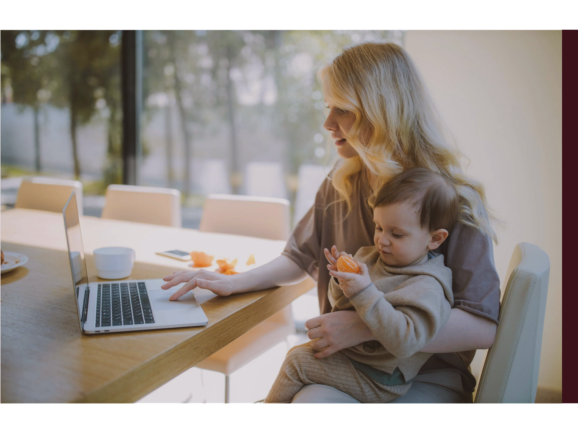 A woman sits at her computer with her baby in her lap multitasking