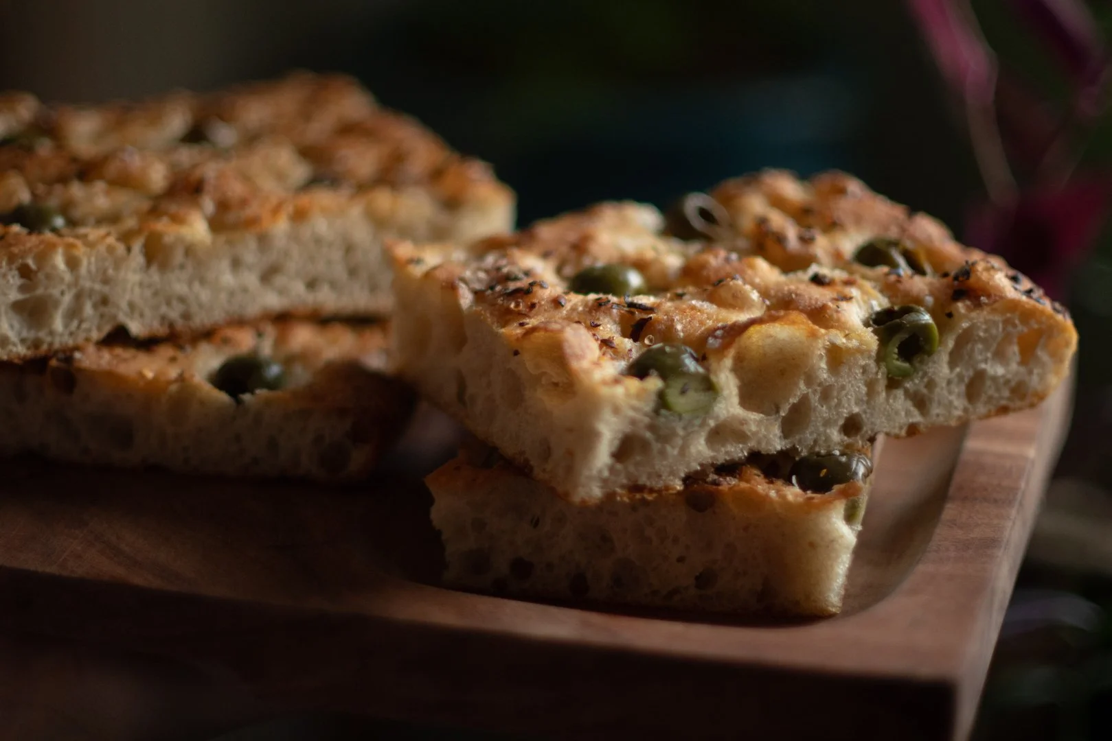 Close-up of two slices of vegetable pizza with green olives on a wooden cutting board.