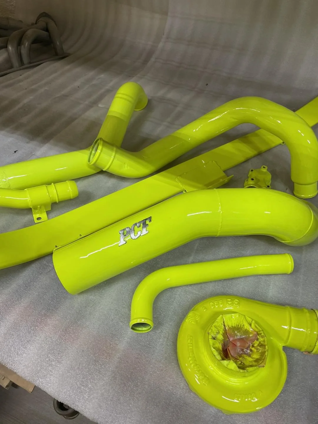 Bright yellow silicone motorcycle exhaust pipes and components with a 'PCF' logo, laid out on a grey fabric-covered surface.