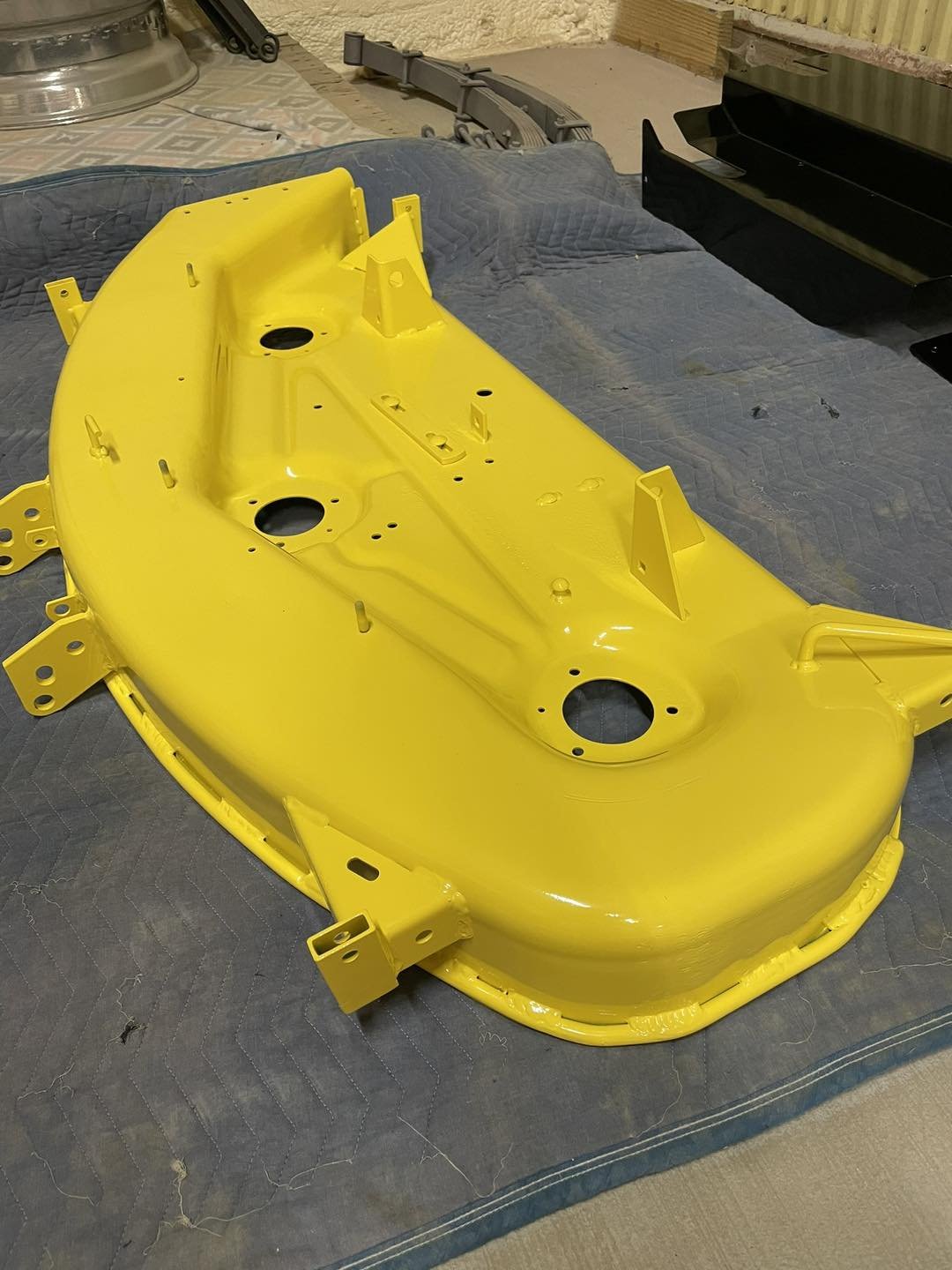 A bright yellow painted motorcycle frame on a padded surface in a workshop setting.