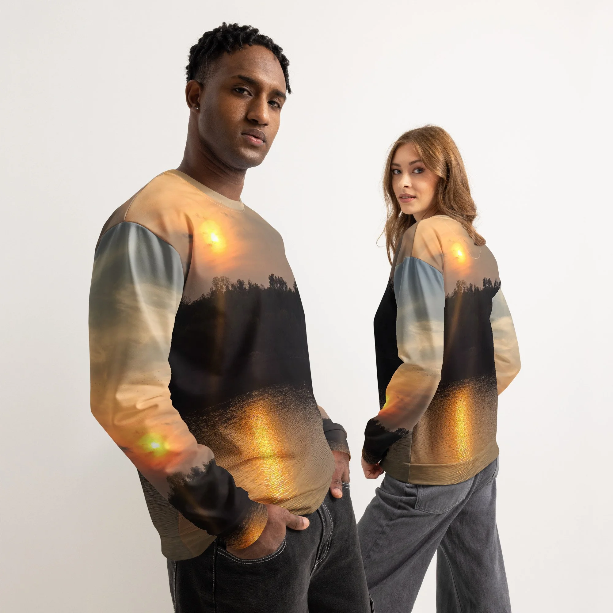 Two models wearing sweatshirts with landscape sunset scenes printed on them, featuring water reflections and trees.