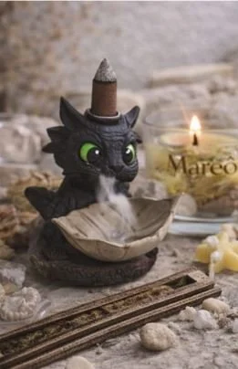 Figura de um dragão com cabeça de papel machê e corpo de brinquedo, com uma vela acesa ao lado, decorando uma caixa de madeira e uma estação de trem de brinquedo.