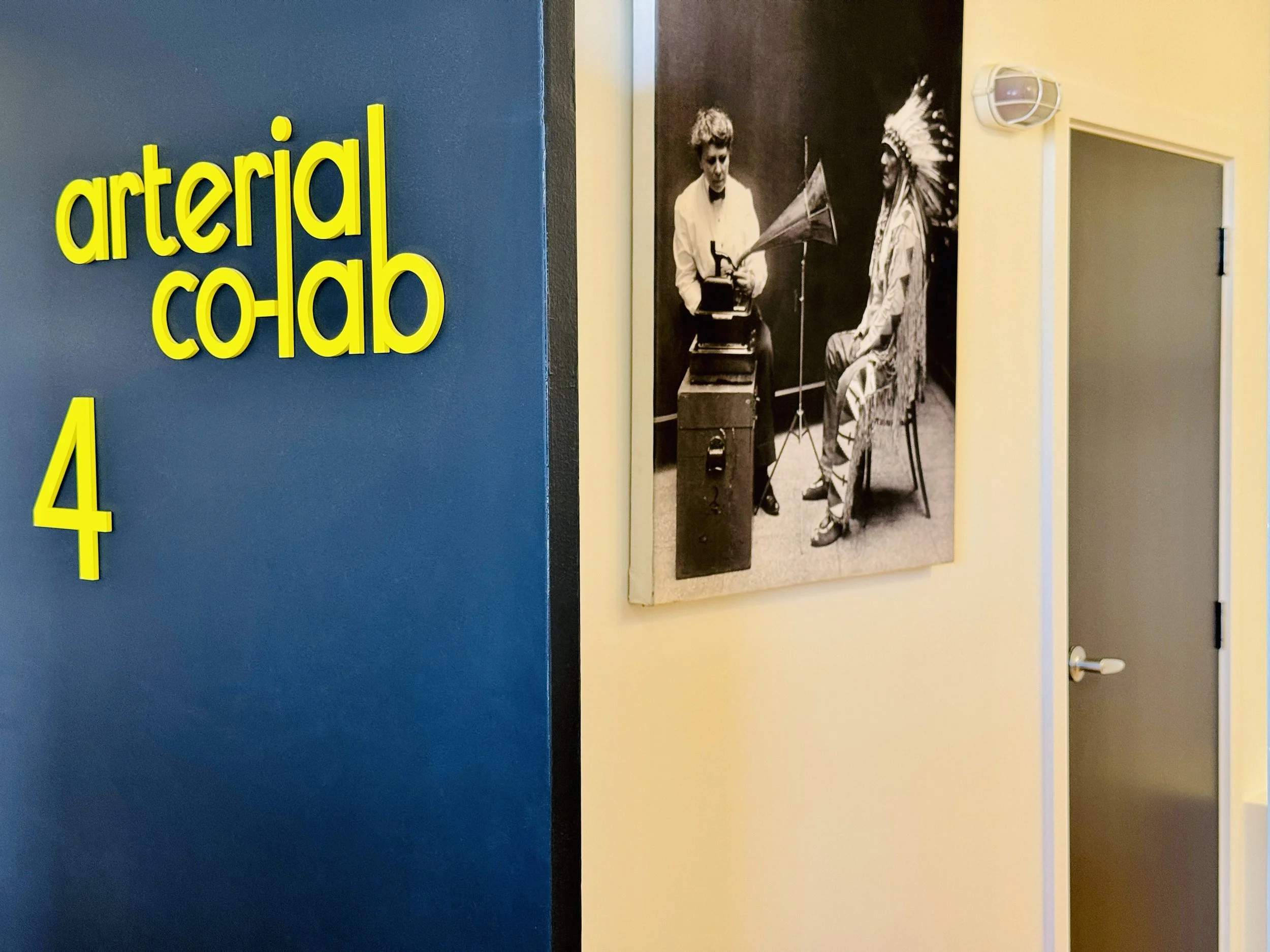 close up of Arterial Colab Studio 4 name on a black door. A photograph of 2 person hanging on the white wall in the background