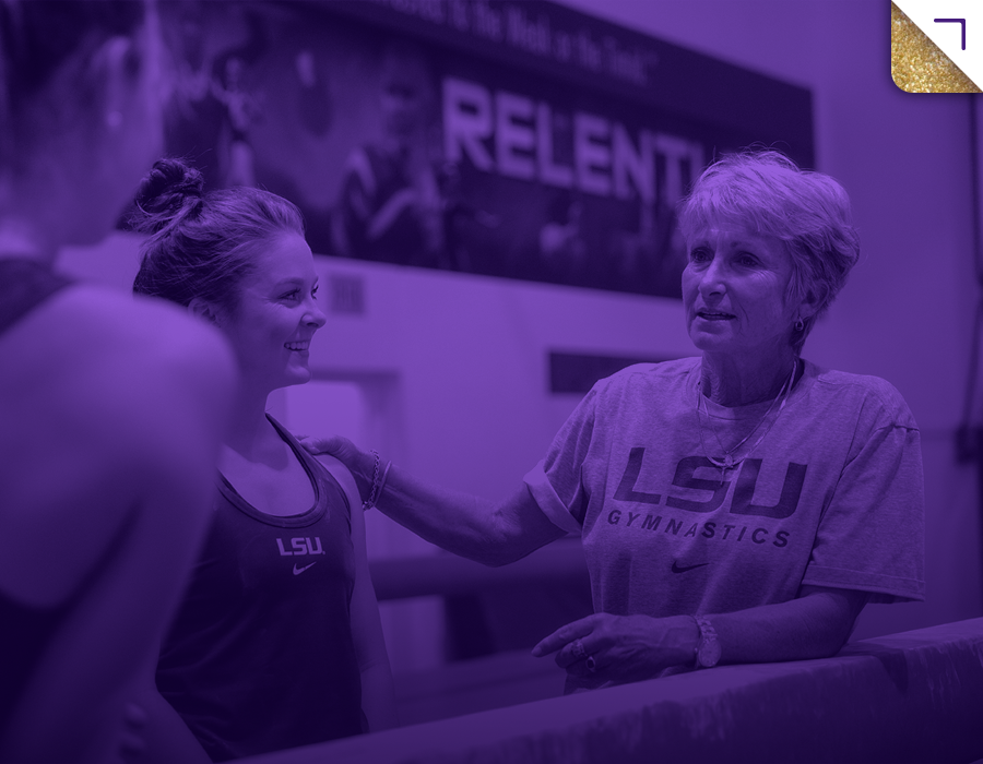 D-D in an LSU Gymnastics shirt talking to a young gymnast with an LSU top, in a gym setting with a supportive atmosphere.