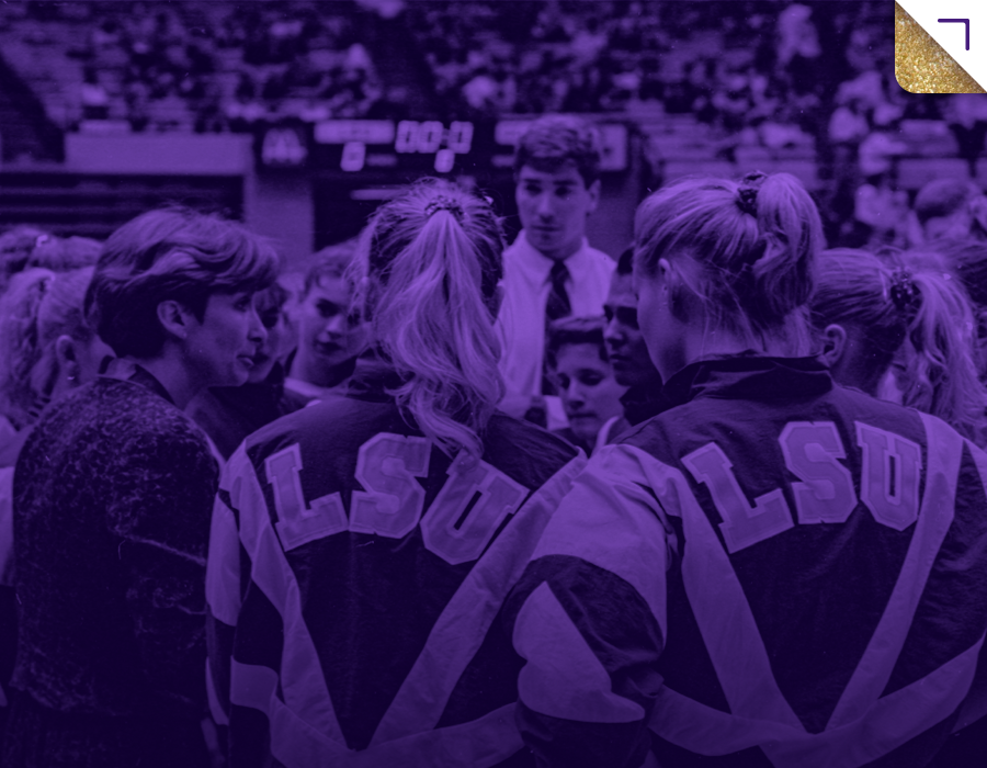 A group of young female athletes in jackets with 'ALSU' written on the back, gathered in a circle talking to a male coach or team leader in a sports stadium.