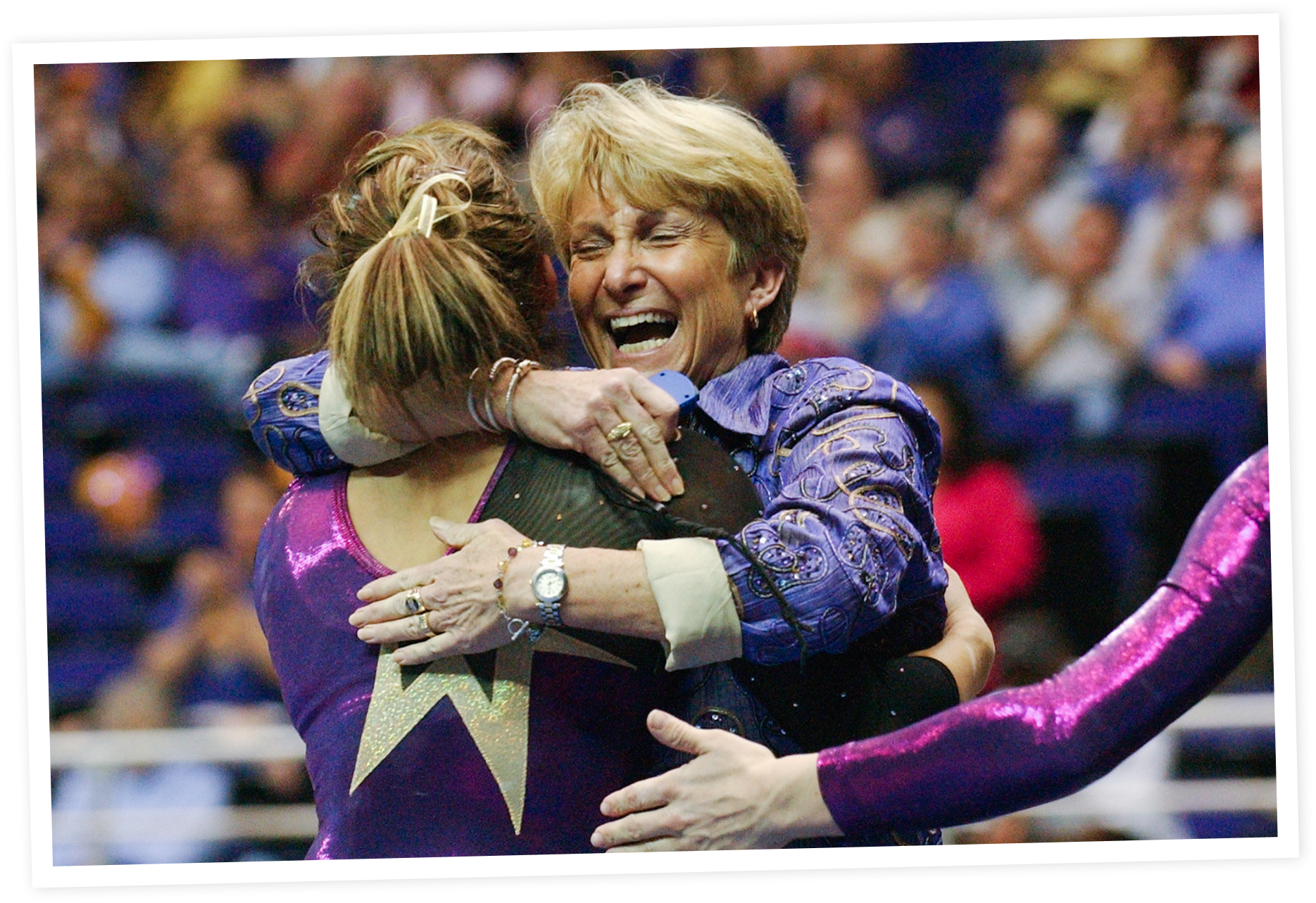 Two women hugging and smiling joyfully at a sporting event, with a blurred crowd in the background.