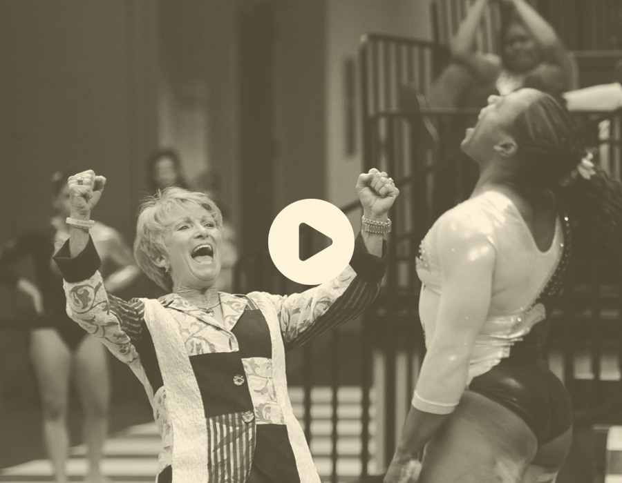 A woman cheerfully celebrating with her fists raised in triumph in a gymnasium or sports arena.
