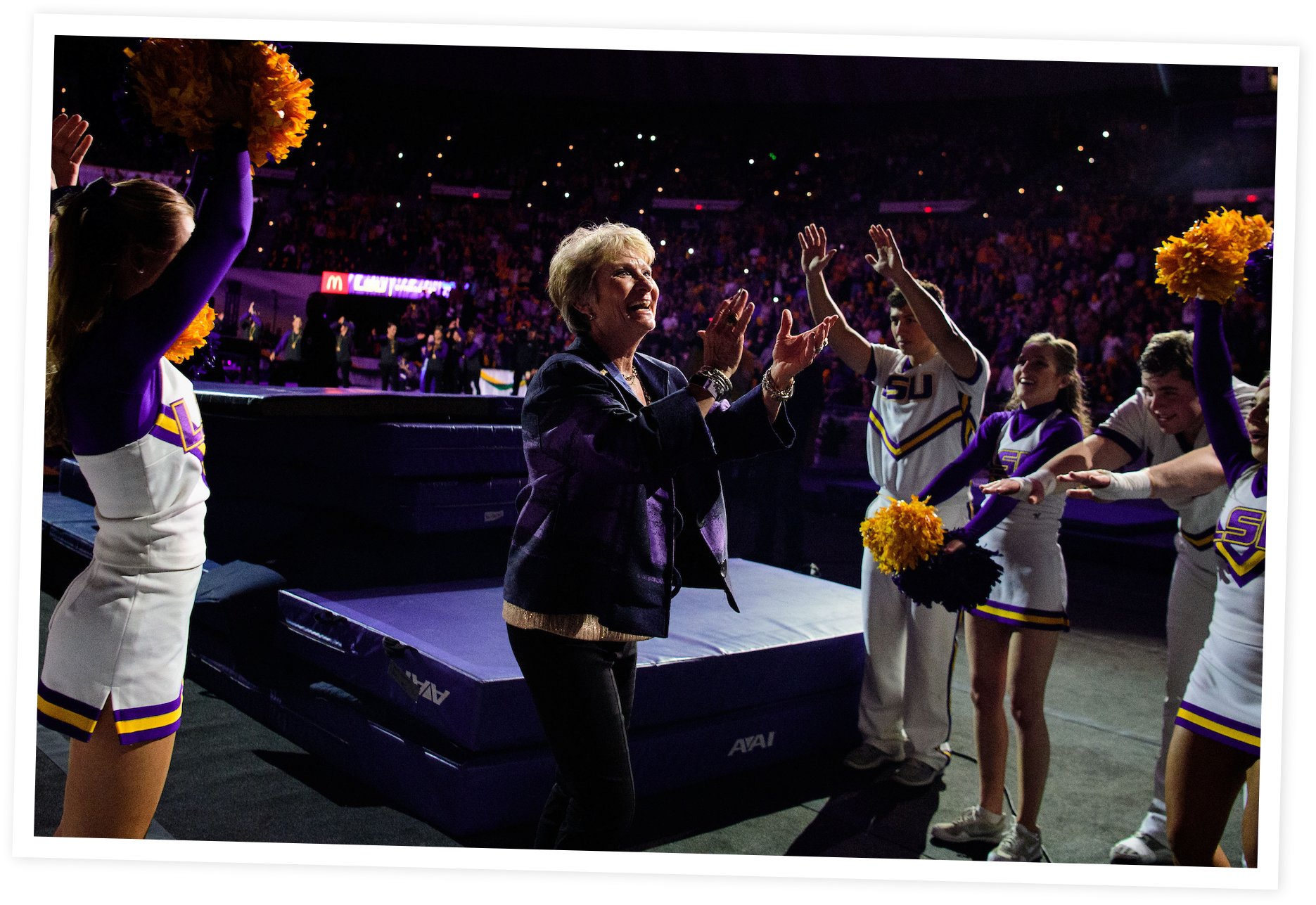 Cheerleaders performing with pom-poms and a woman, possibly a coach or team member, clapping on a sports arena court.