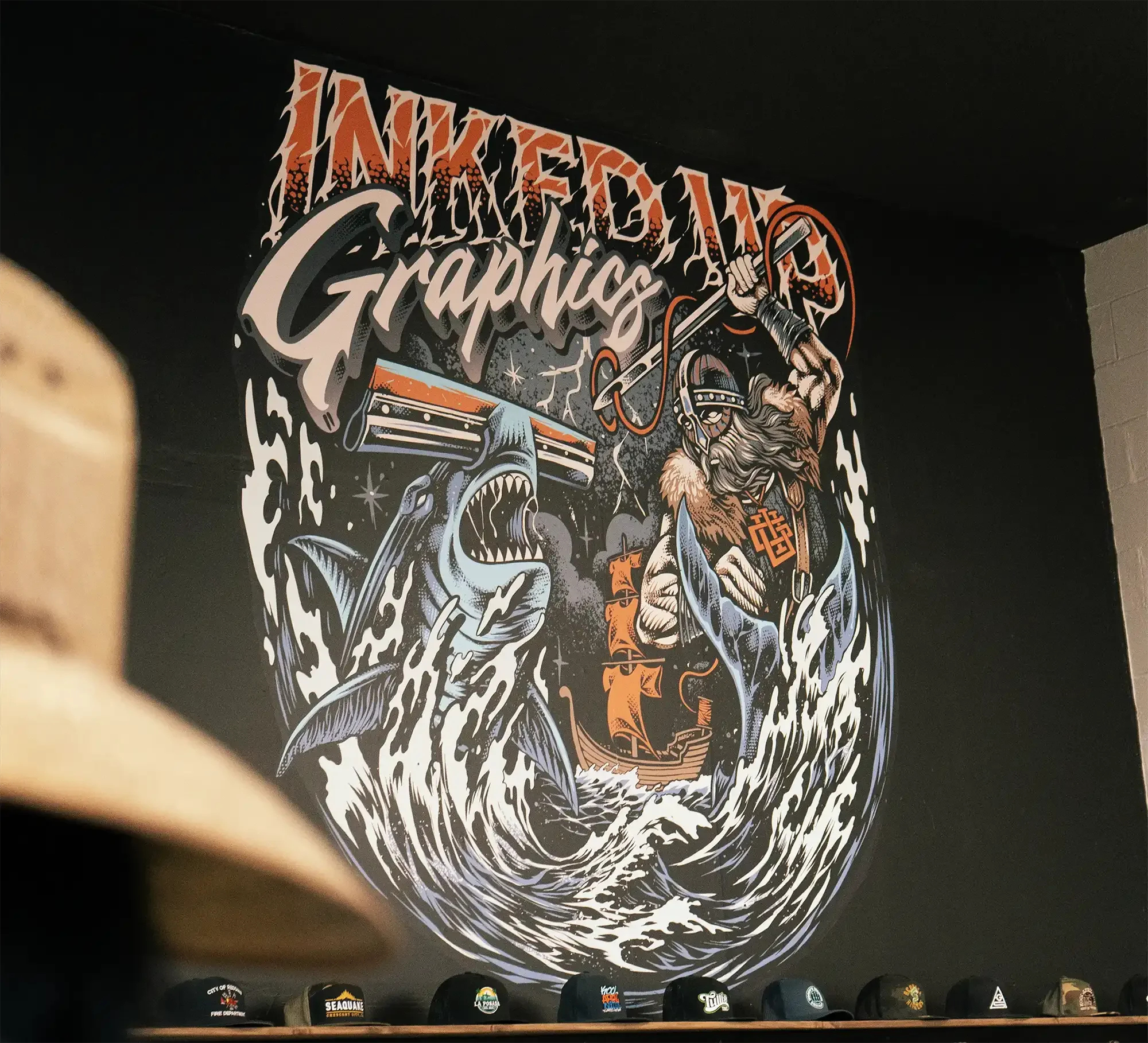 A mural with the words 'Innovative Graphics' and a pirate holding a hook and sword, attacking a large shark that is breaching the water, with a ship in the background.