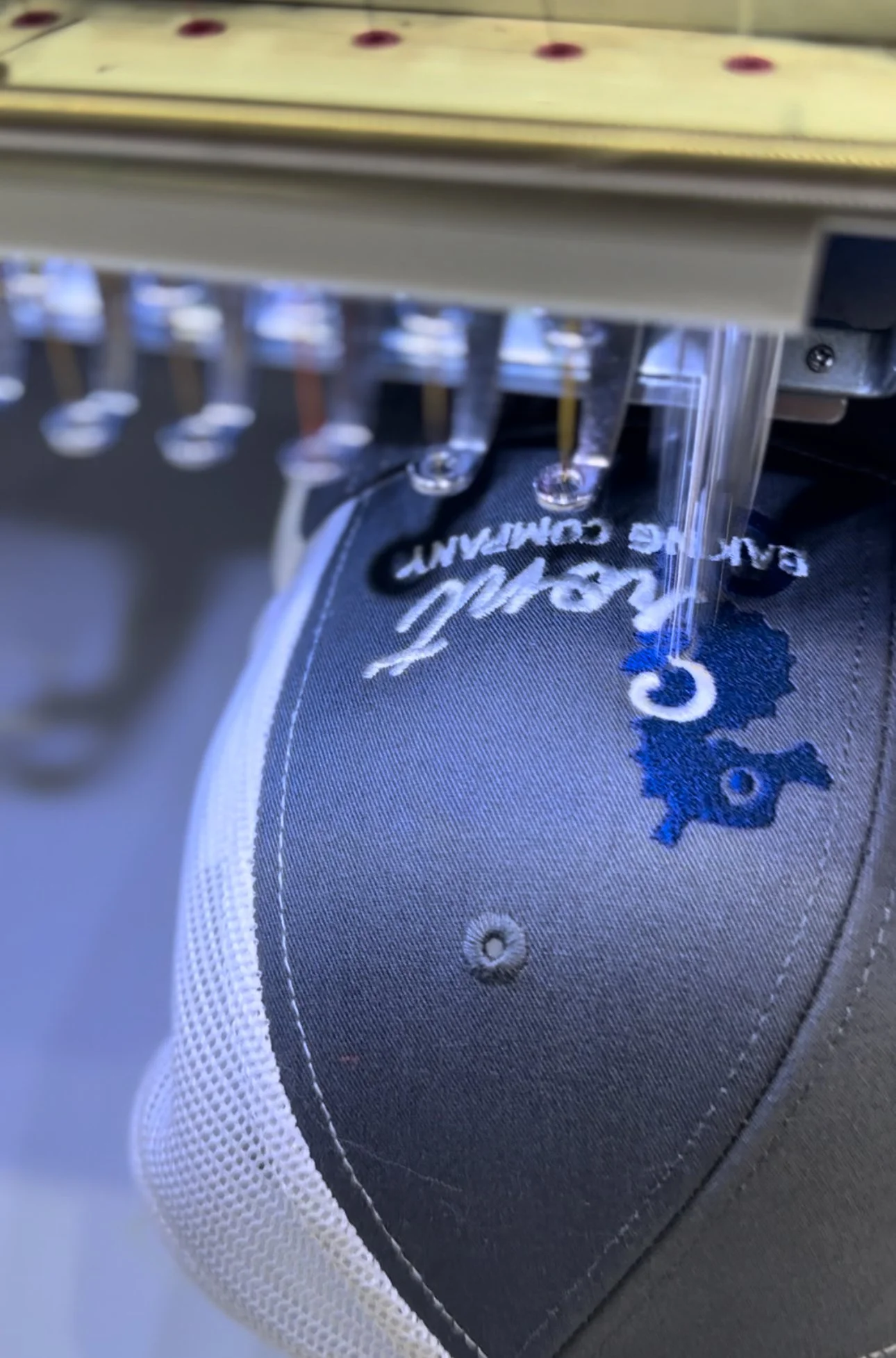 Close-up of a embroidery machine stitching a design onto a gray and black fabric shoe with white trim.