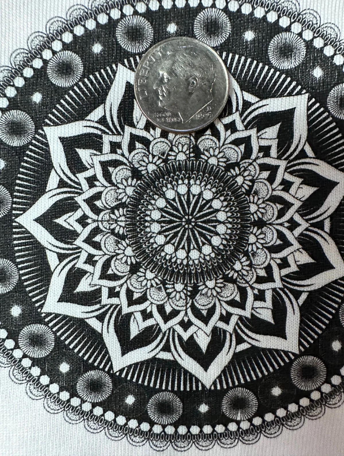 Close-up of a black and white mandala pattern with a quarter coin placed on top for scale.