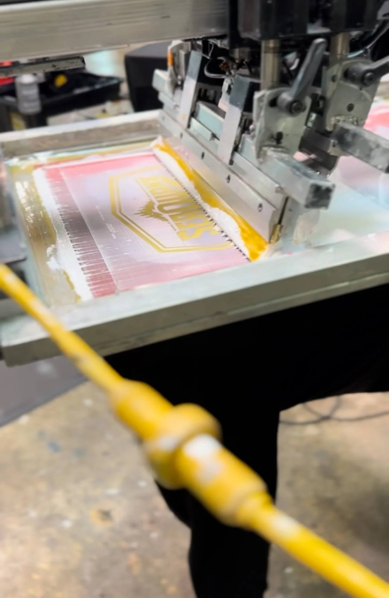 Close-up of a printing machine with a partially printed sheet featuring a gold and pink design.