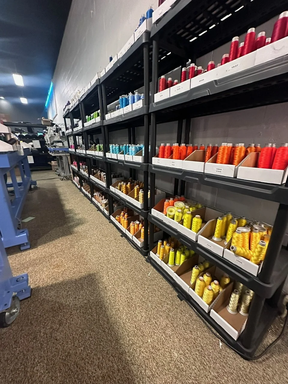 Shelf filled with colorful spools of thread in various colors including red, blue, green, orange, yellow, and brown, in a store or sewing supply shop.