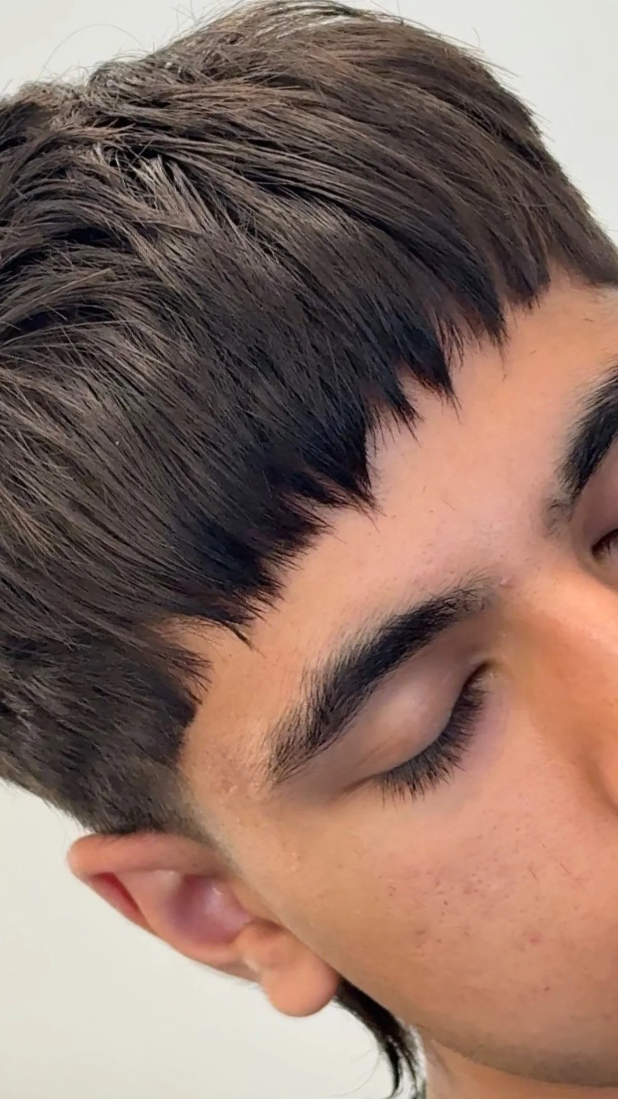 Close-up of a person's face with eyes closed, showing dark hair, eyebrows, and part of the ear.