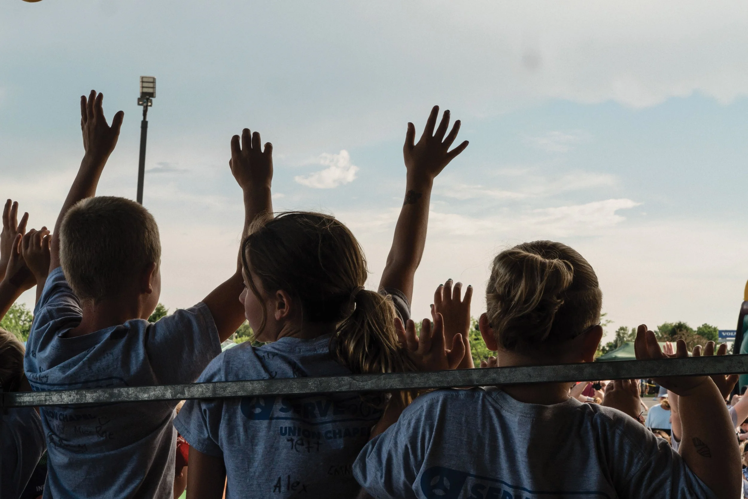 Children raise their arms up in a sign of worship outdoors.