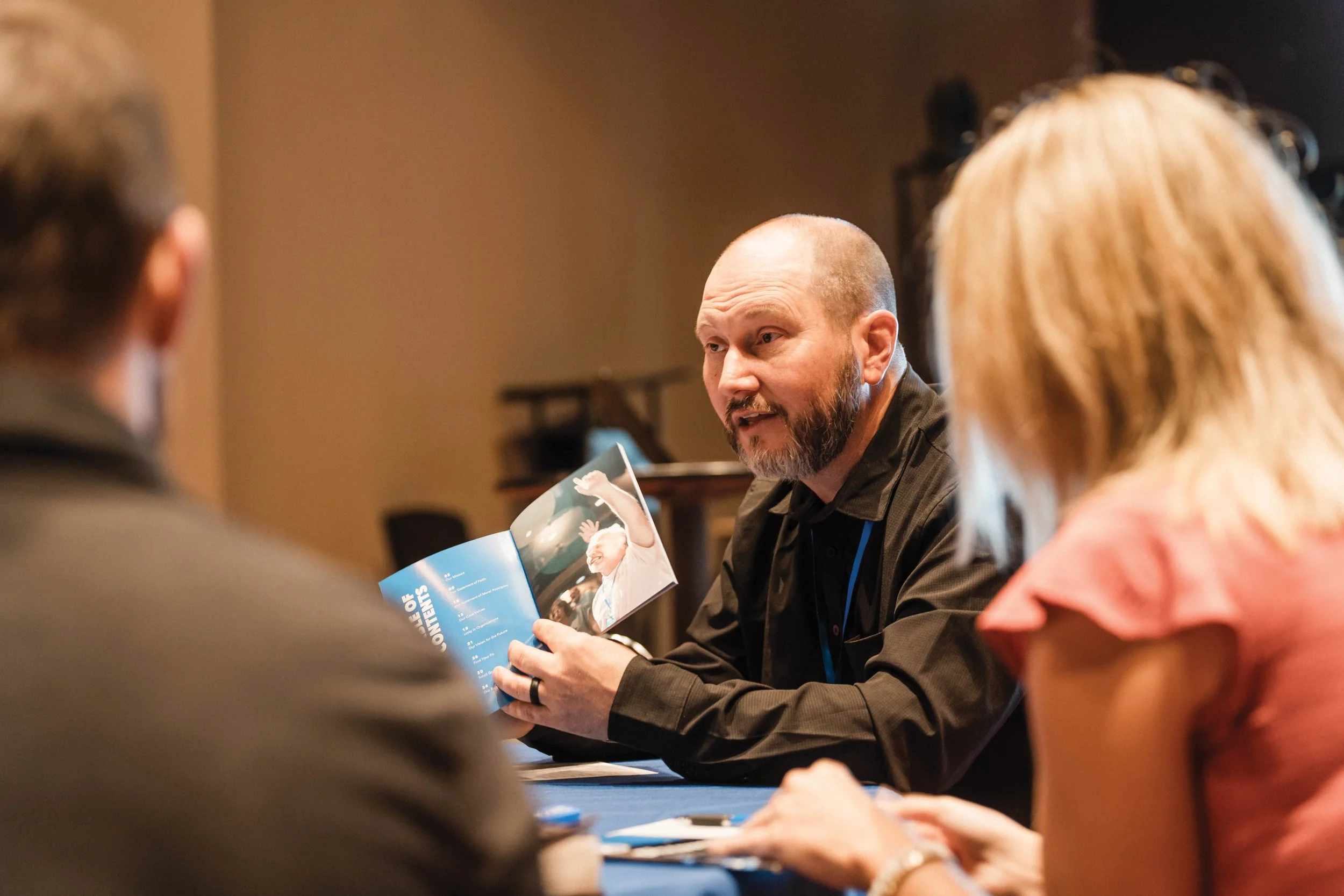 Pastor Jeff Hughes sits with parishioners at a table pointing to a booklet.