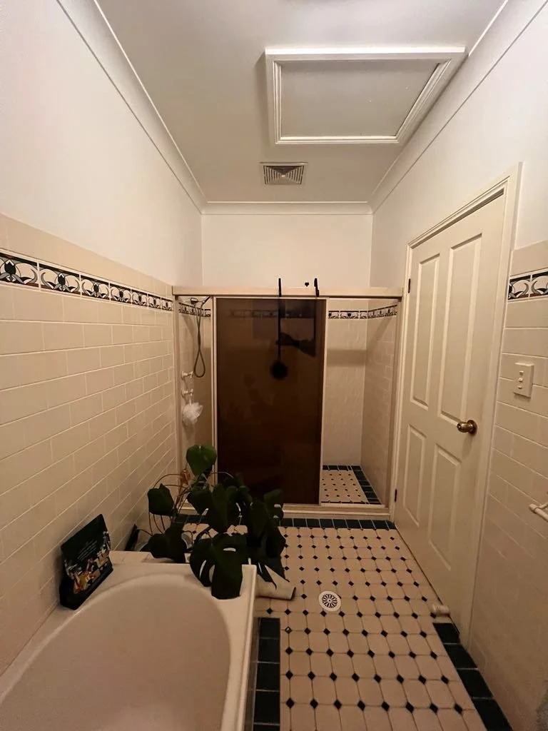 Before image of a 90s style bathroom featuring outdated tiles, small shower with dark screen and old faucets