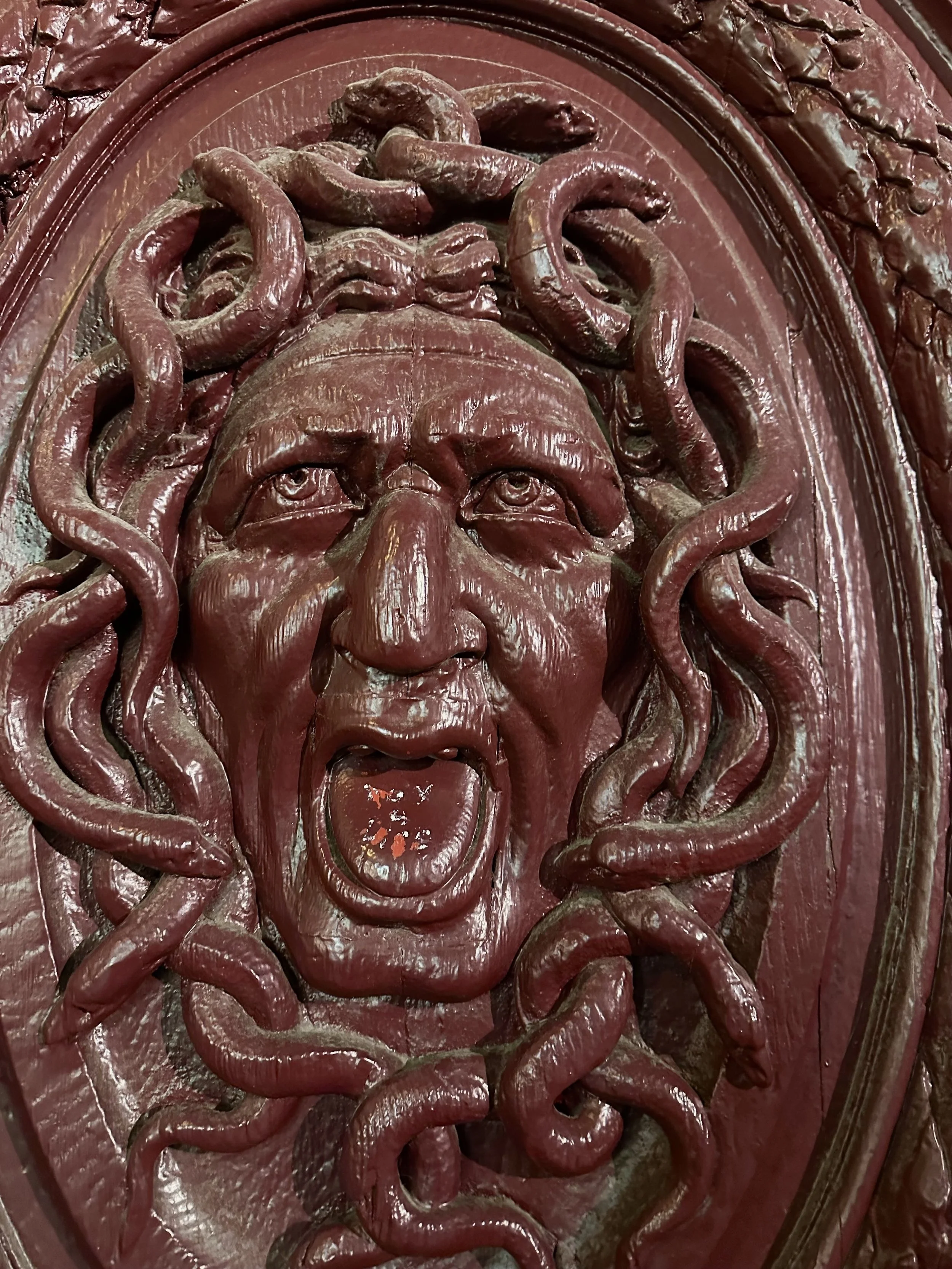 A detailed red sculpture of a face with an angry expression, mouth open, surrounded by serpents.