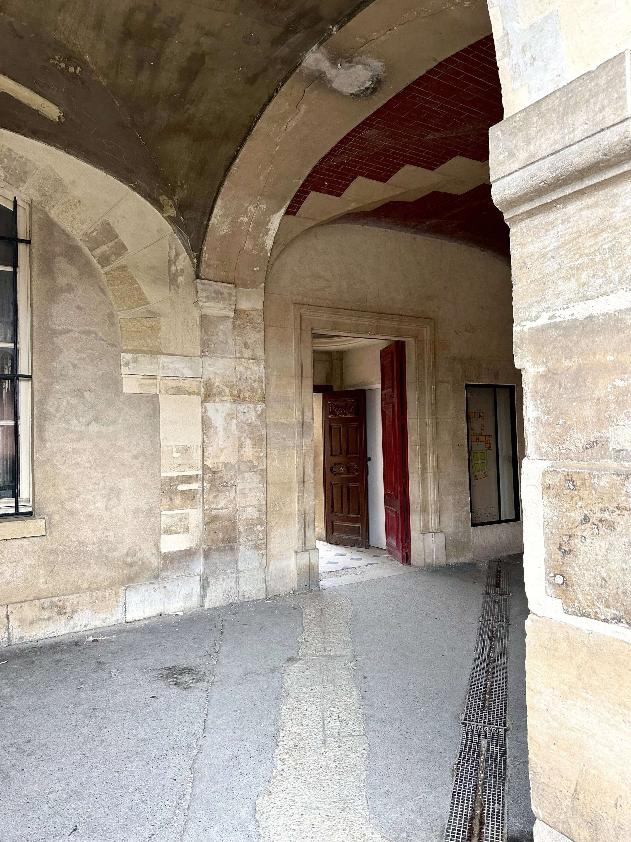 Stone arches and walls with an open doorway and red door in the background.