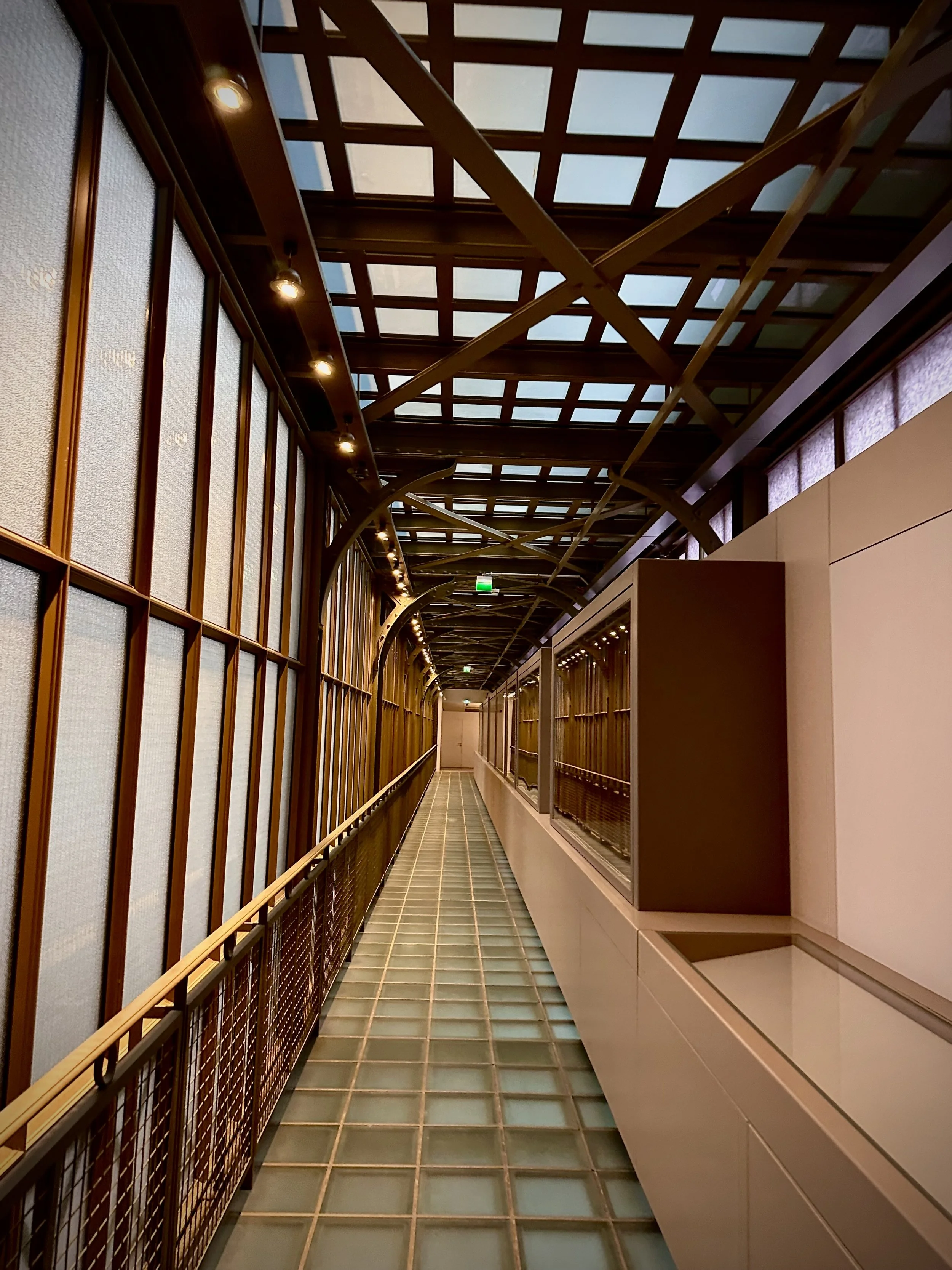 Indoor walkway with glass block flooring, wooden wall panels, and a ceiling with a grid pattern and exposed beams.