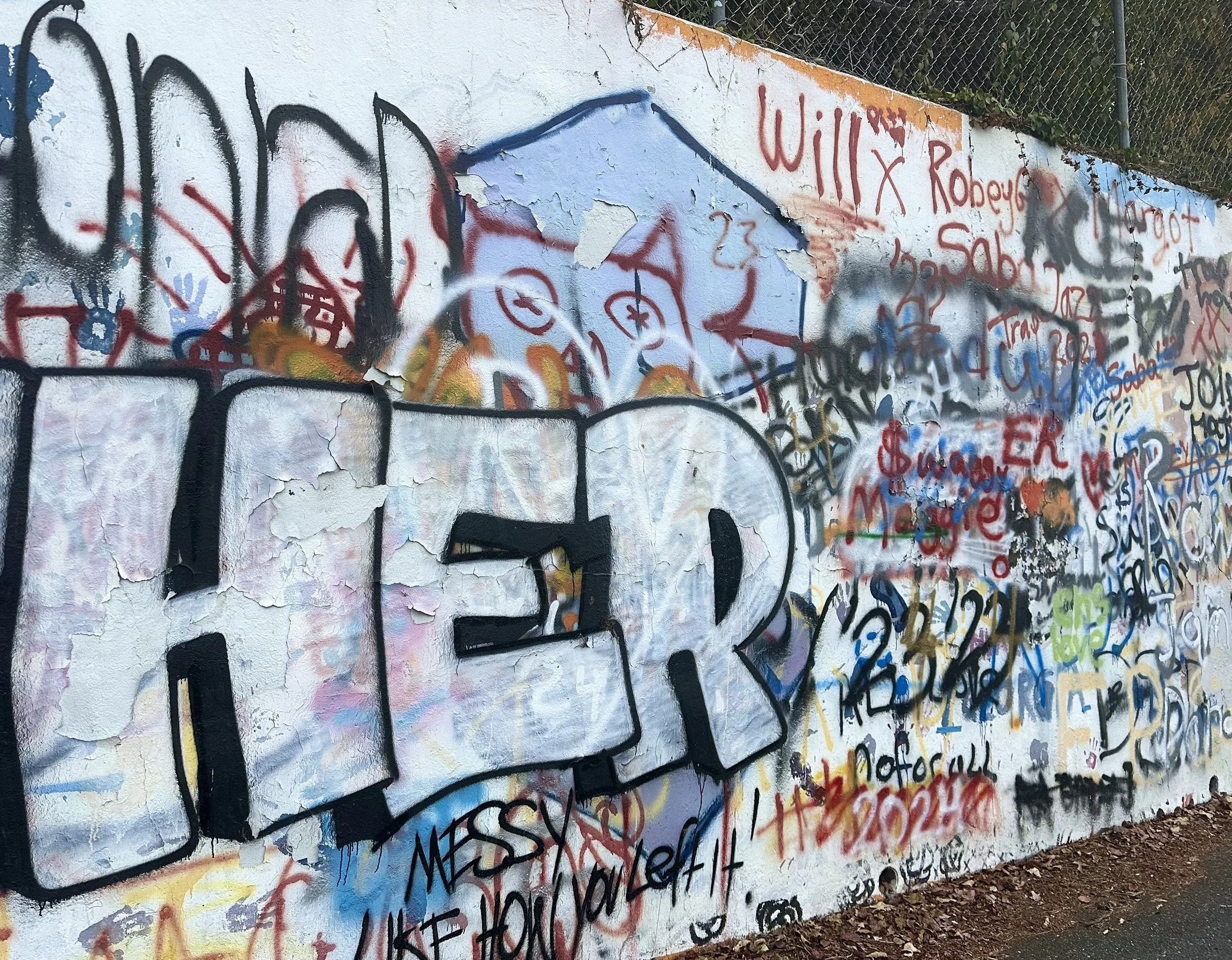Colorful graffiti wall with various tags, doodles, and messages, including a large white and black piece in the front.