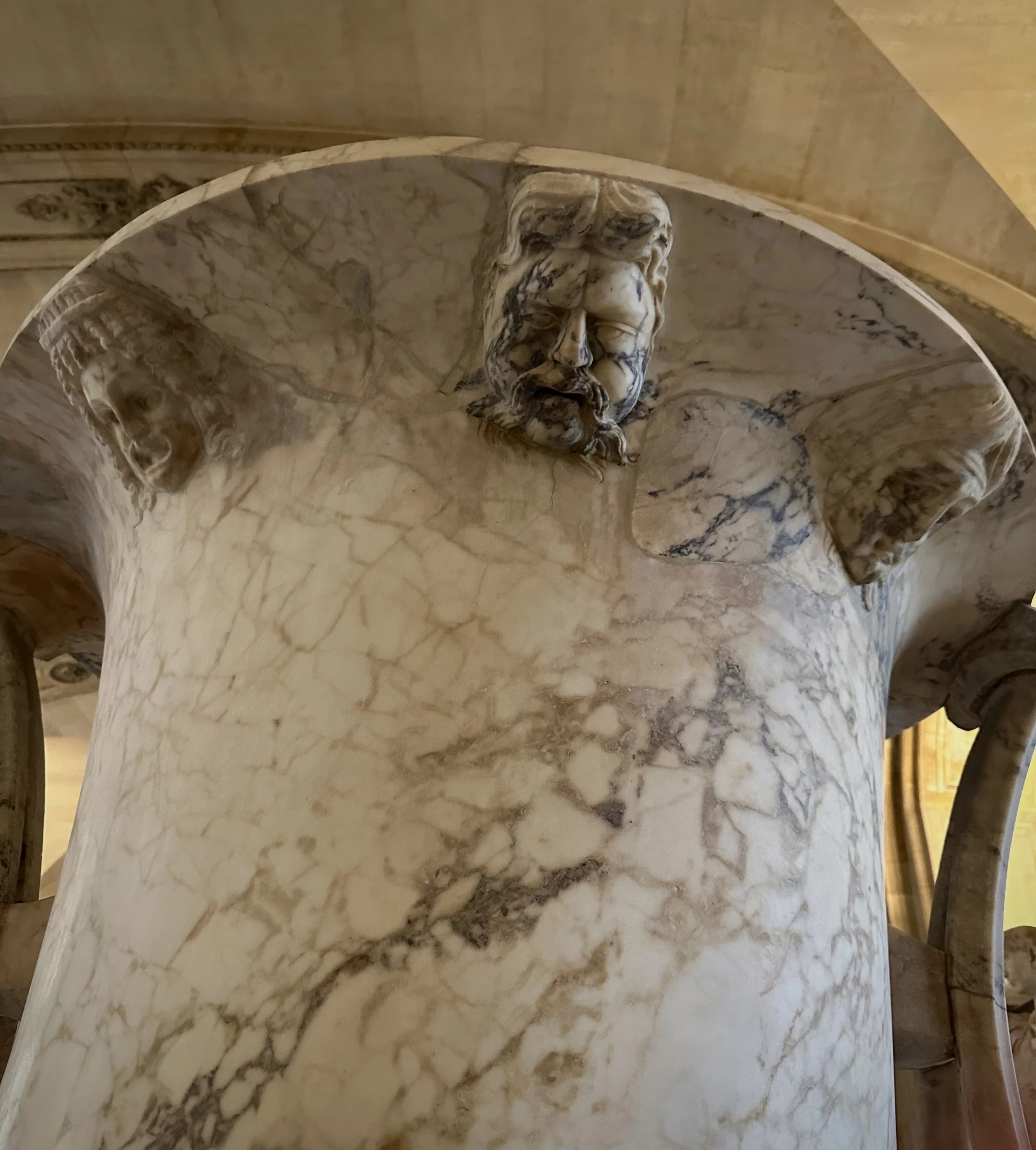 Marble column with carved marble sculptures of male heads at the top.