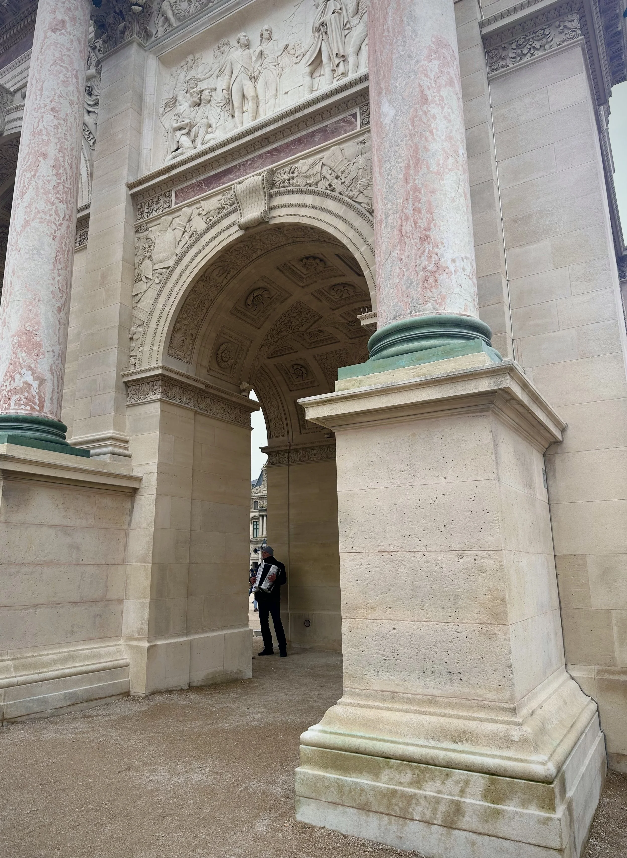 Close-up of an ornate stone archway with detailed carvings and large marble columns, with a person standing underneath.
