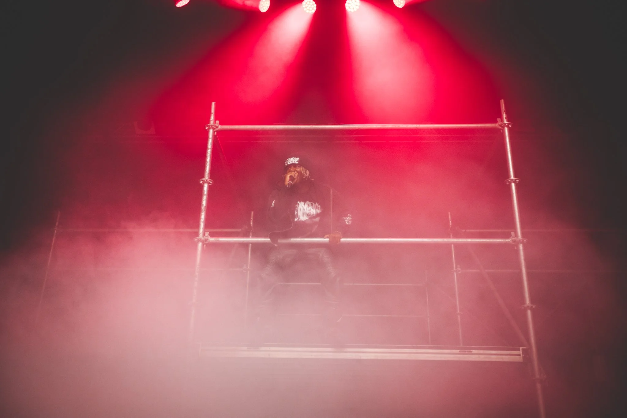 Performer on a scaffold stage illuminated by red spotlights during a concert or performance.