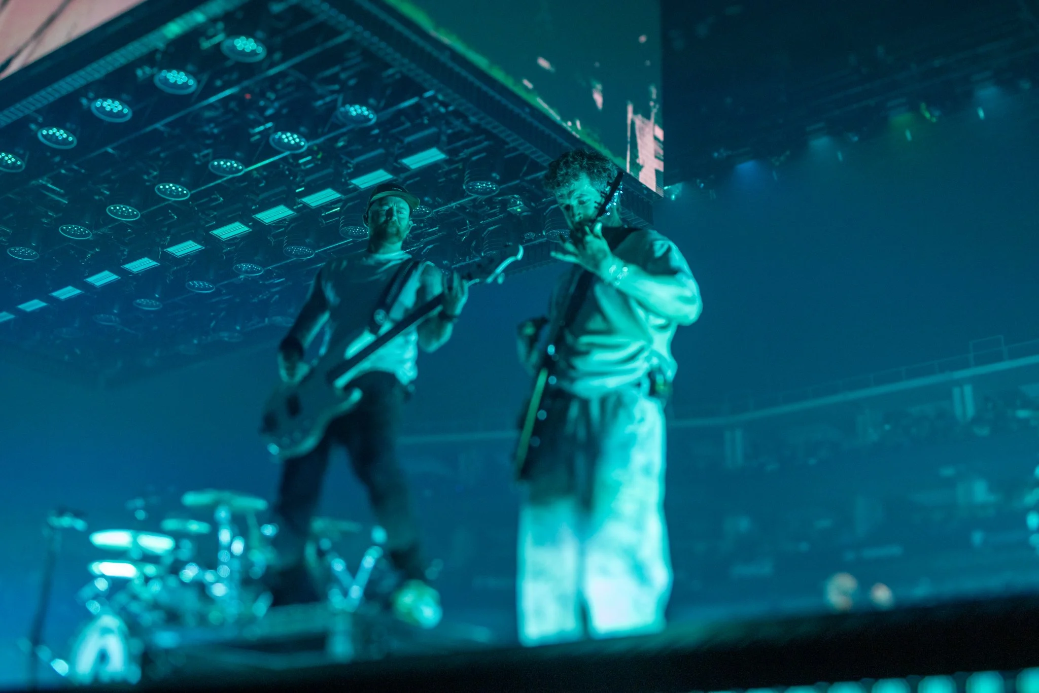 Two musicians performing on stage with blue lighting and electronic equipment in the background.