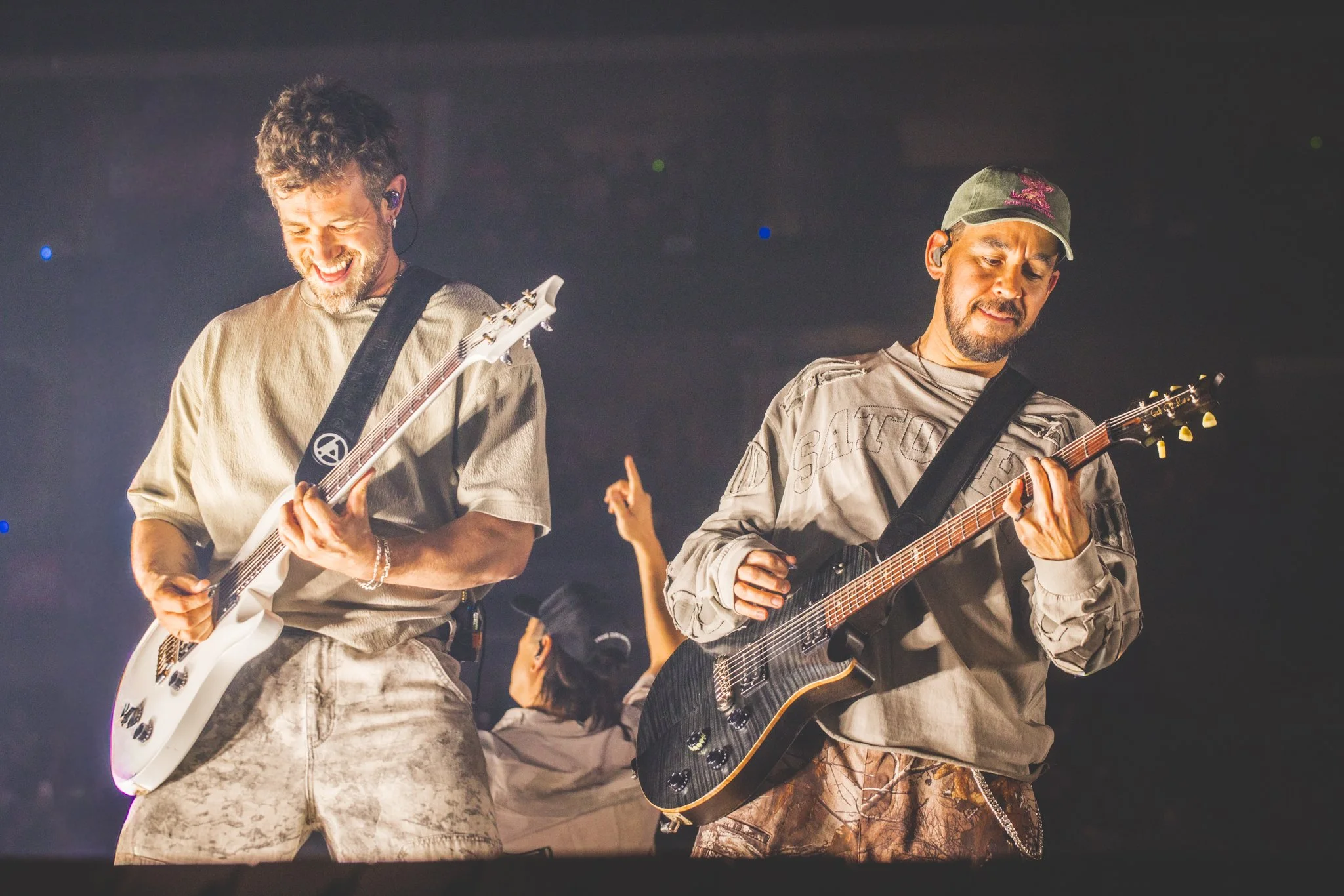 Two men playing electric guitars on stage during a concert, smiling and enjoying the music.
