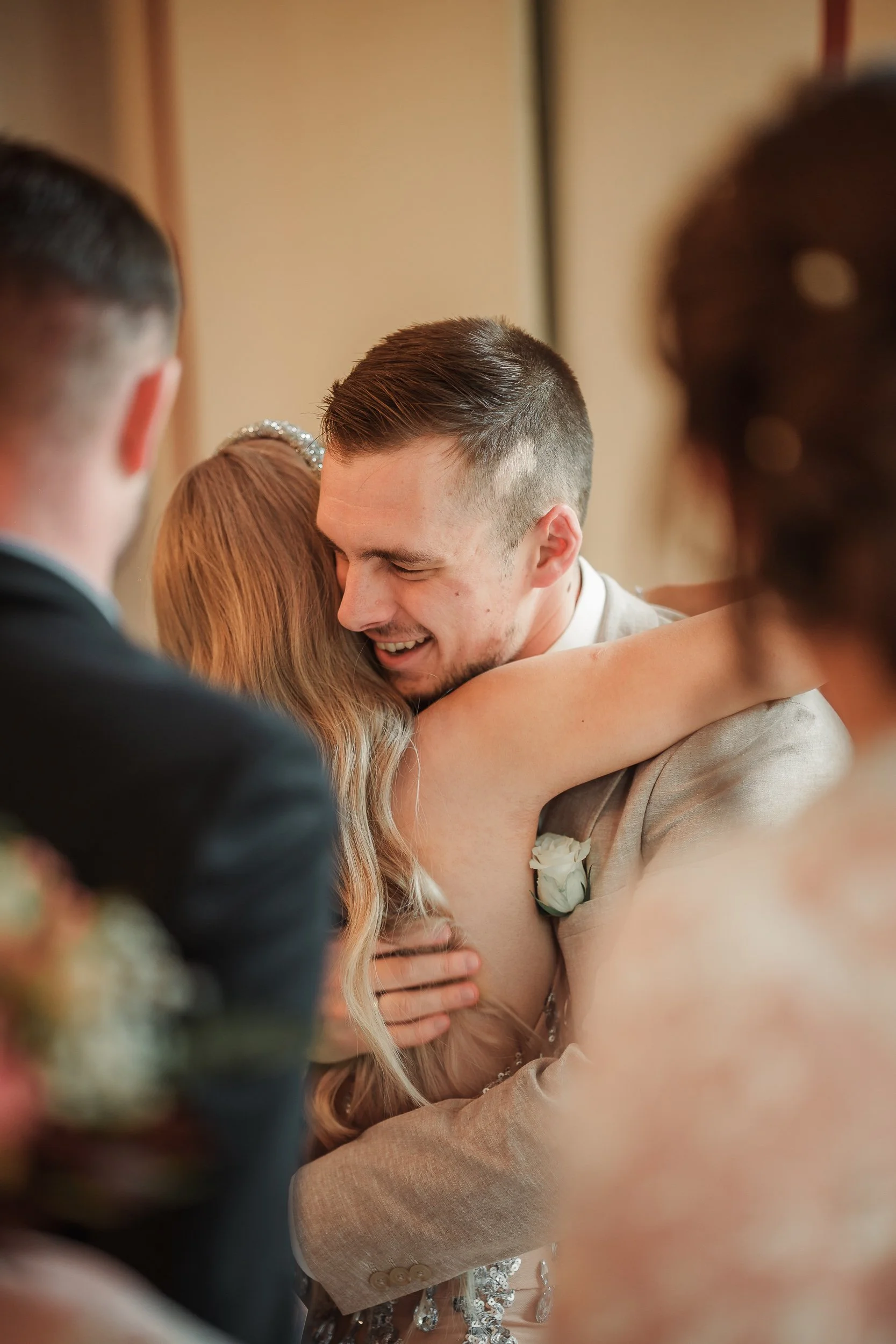 Ein Mann und eine Frau umarmen sich bei einer Hochzeit, alle anderen Personen sind im Hintergrund unscharf.