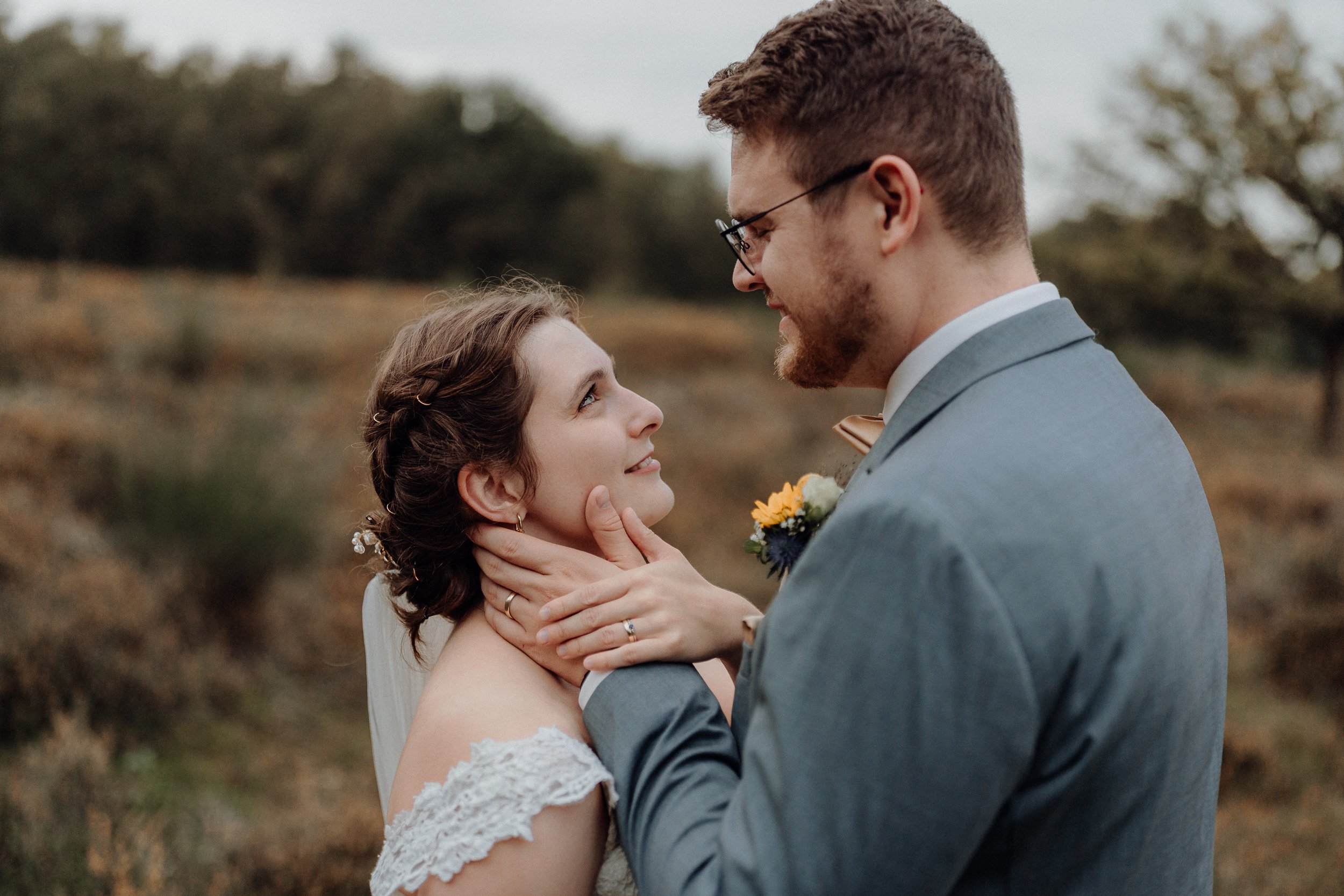 Ein Brautpaar während der Hochzeitszeremonie im Freien, das sich liebevoll ansieht, mit Naturhintergrund und Bewölktem Himmel.