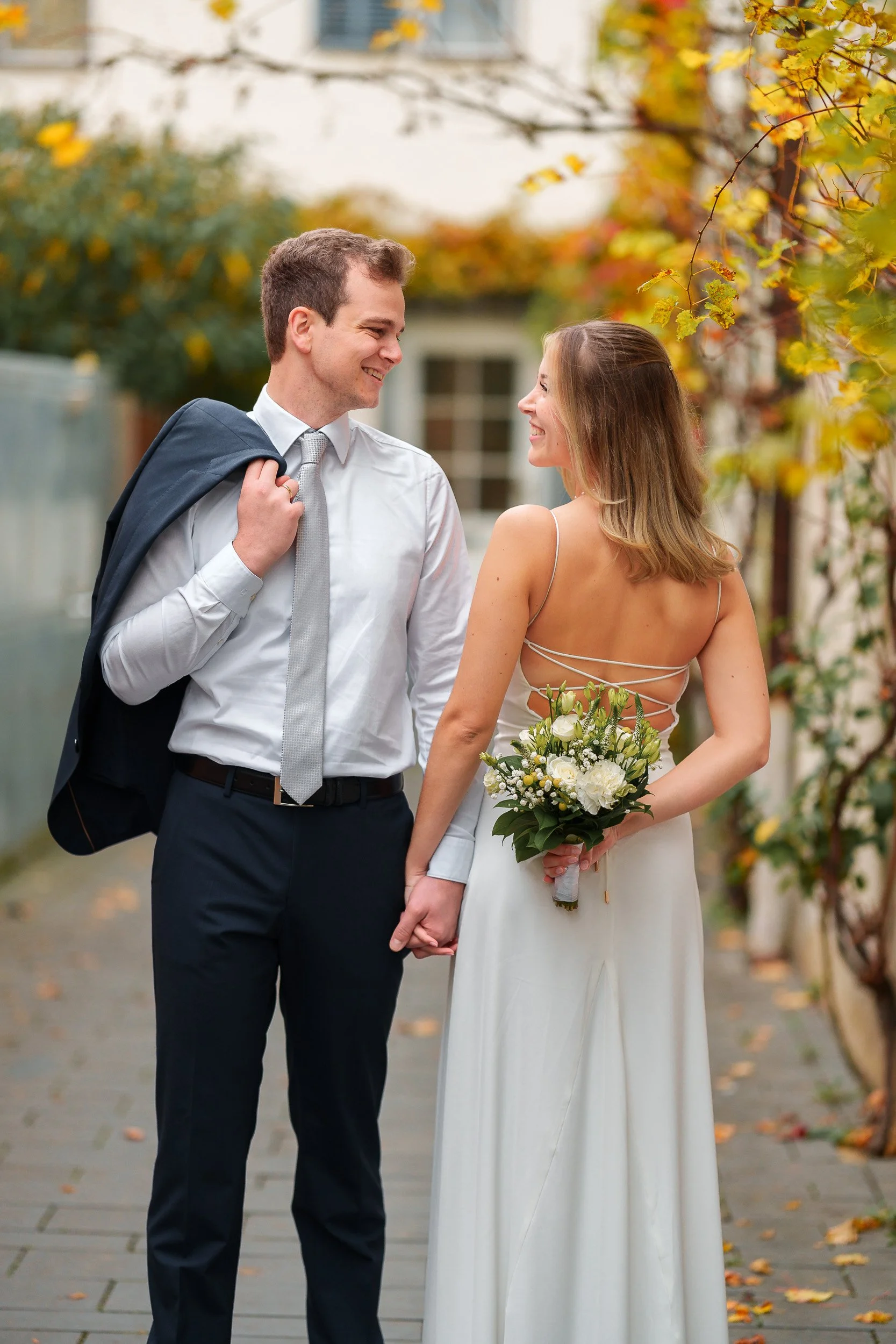Ein Paar, ein Mann und eine Frau, stehen sich liebevoll gegenüber, während die Frau eine Brautstrauß hält. Es ist Herbst, mit gelben und orangefarbenen Blättern im Hintergrund.