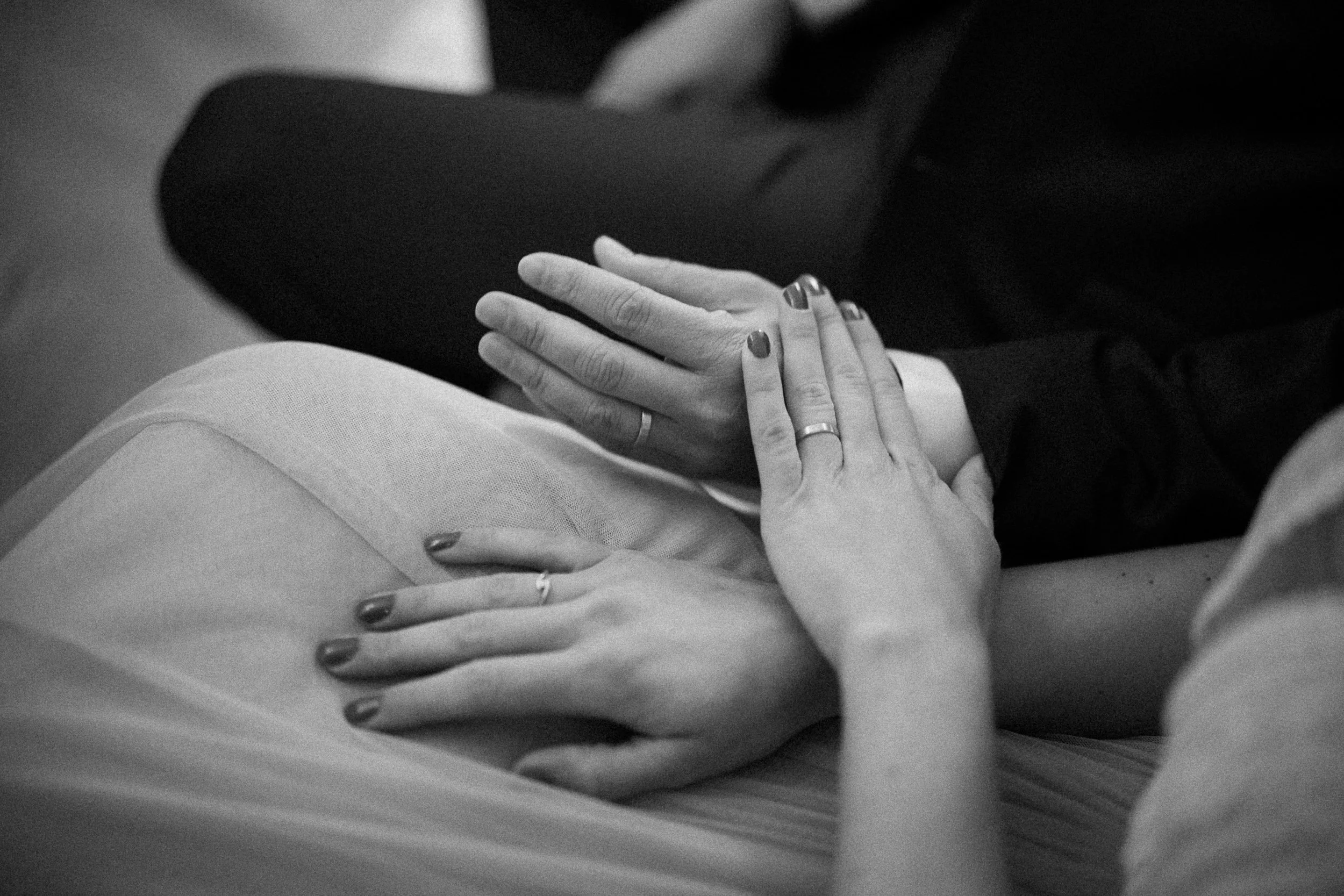 Nahaufnahme von Händen mit Ringen, die auf dem Schoß ruhen, in Schwarz-Weiß.