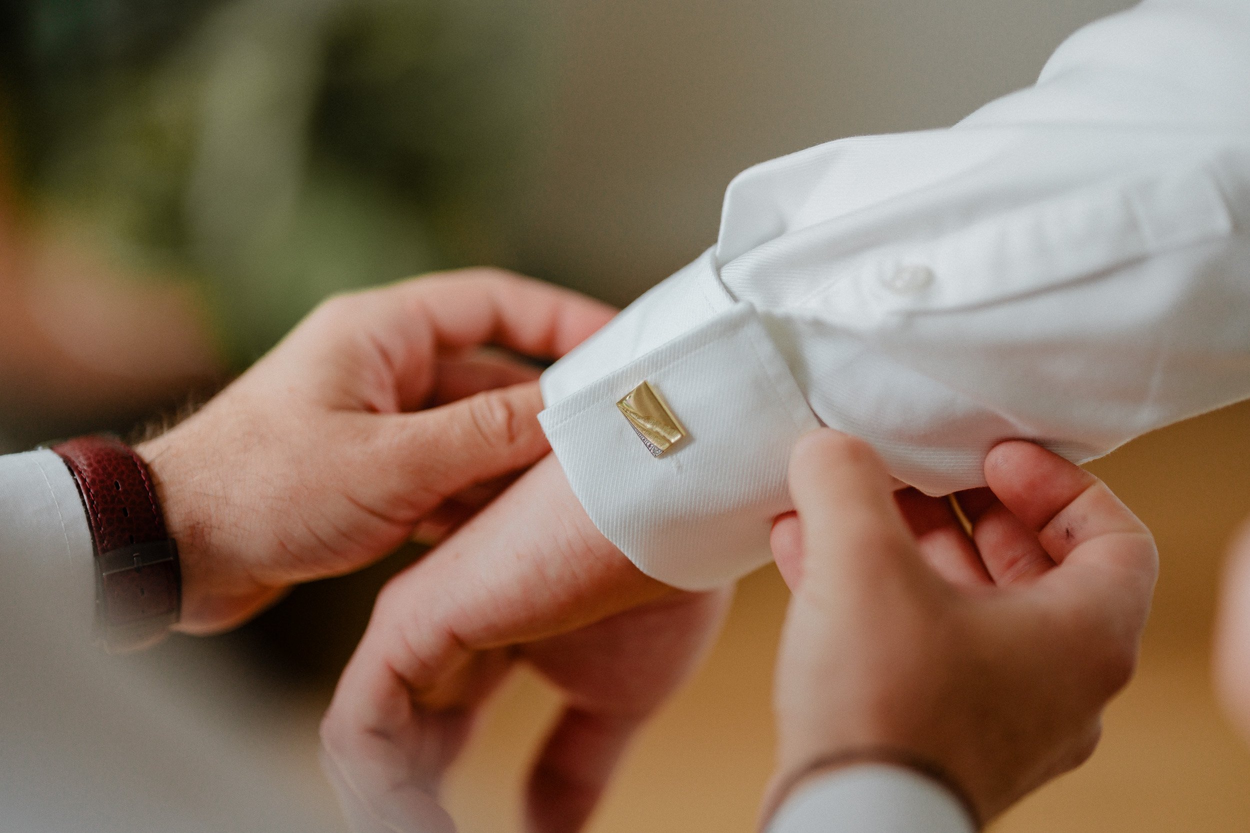 Nahaufnahme der Hand eines Mannes, der die Manschette eines weißen Hemdes mit einem goldfarbenen Manschettenknopf befestigt.