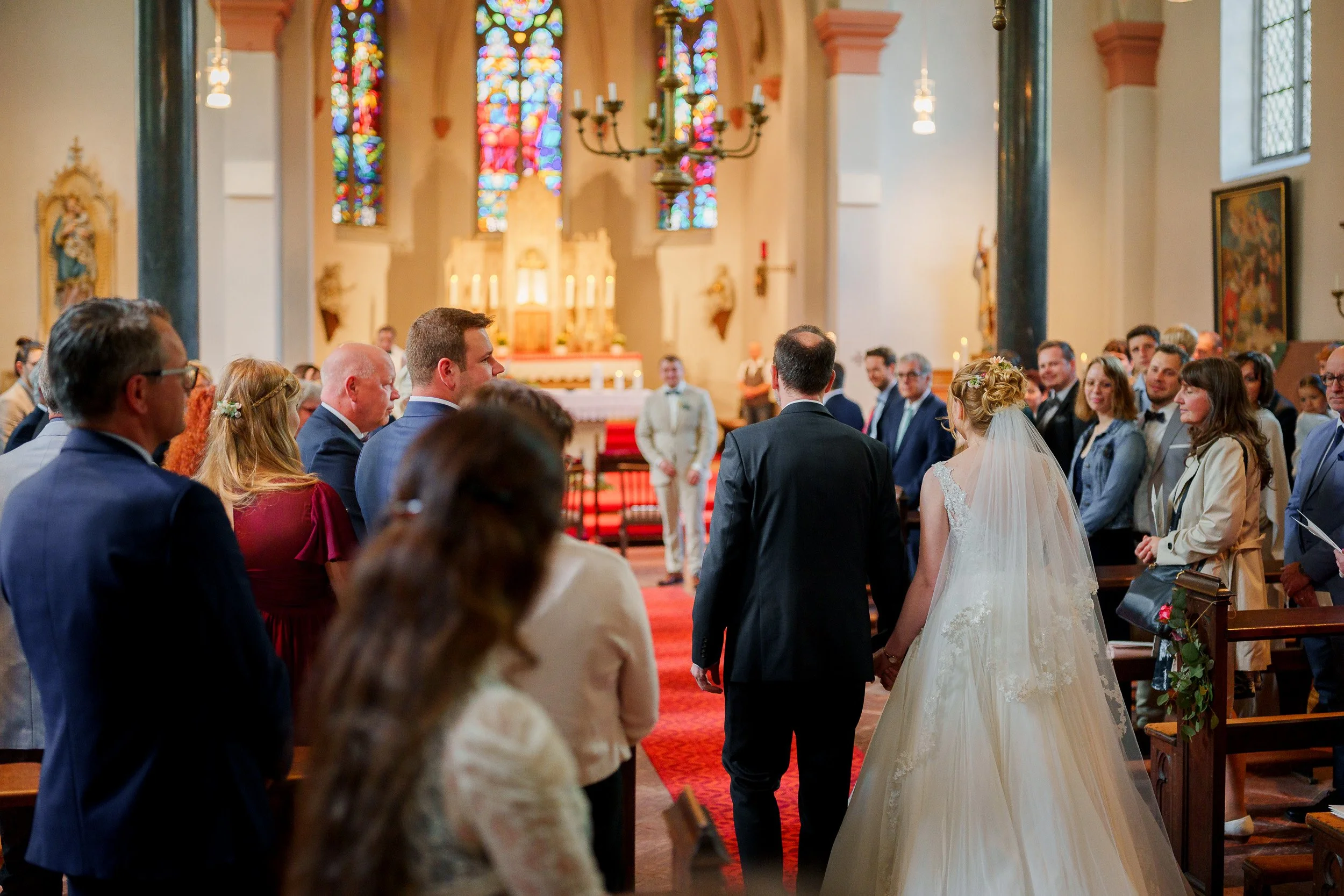 Braut und Bräutigam stehen in einer Kirche, umgeben von Gästen, während sie den Trauungsgelöbnissen zuhören.
