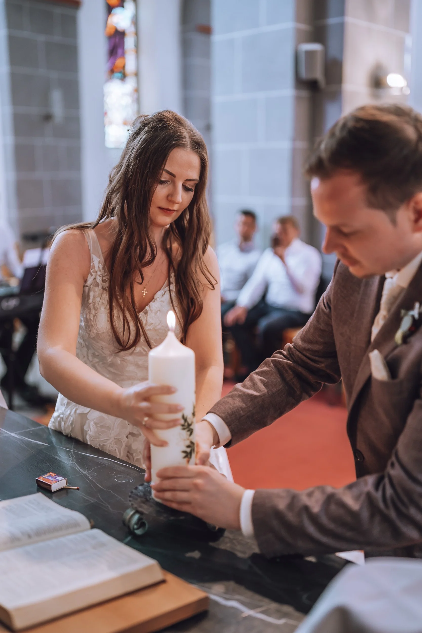 Ein Brautpaar bei einer Zeremonie, bei der eine Kerze entzündet wird, vermutlich ihre Hochzeitszeremonie in einer Kirche.