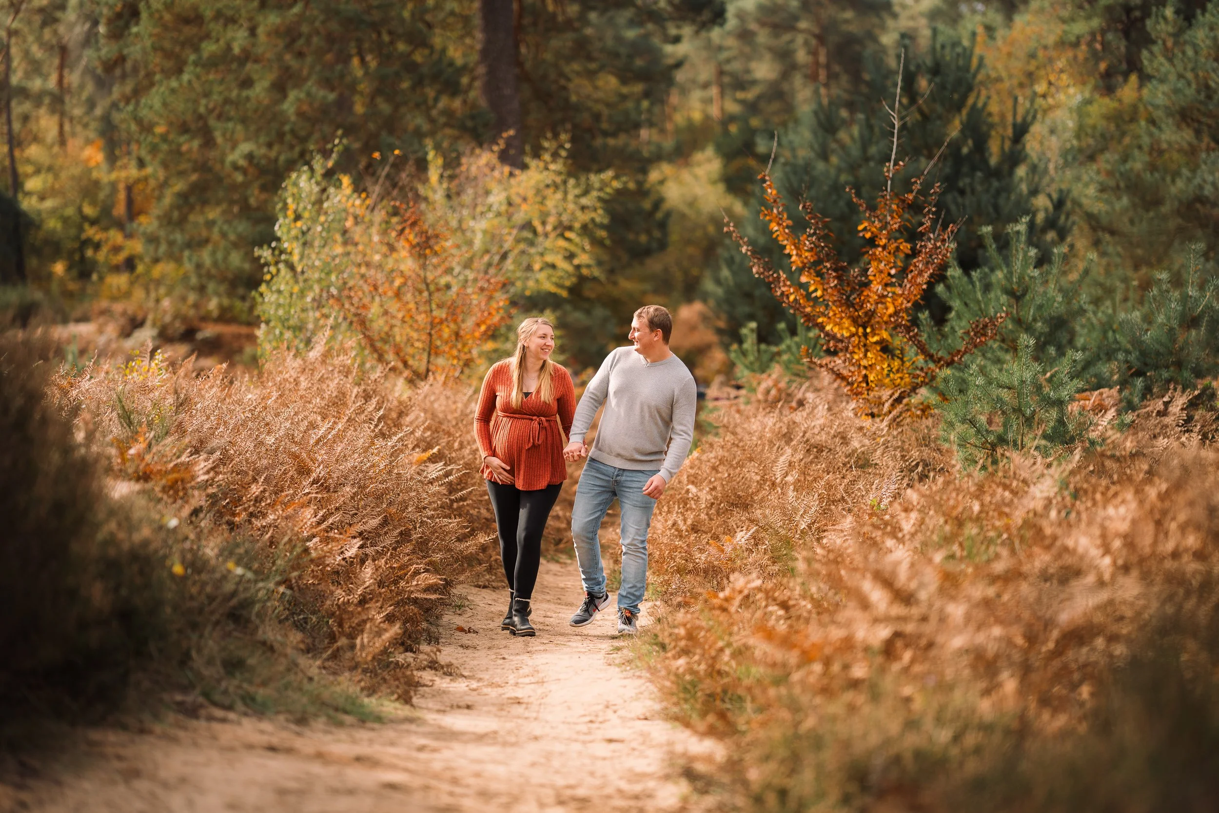 Ein Paar geht Hand in Hand durch einen herbstlichen Waldpfad und lacht.