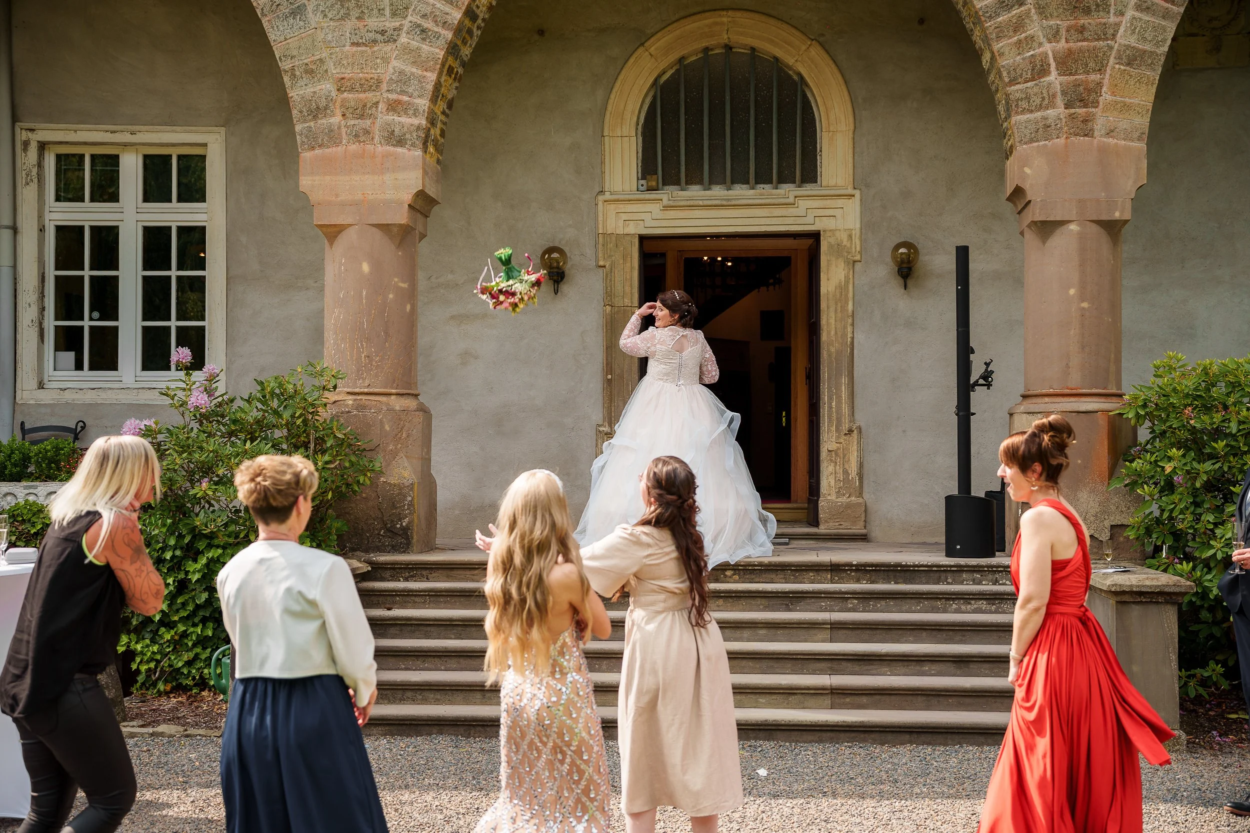 Hochzeit mit Braut, die ihre Schuhe von den Stufen einer alten Villa trägt, umgeben von Gästen im Freien