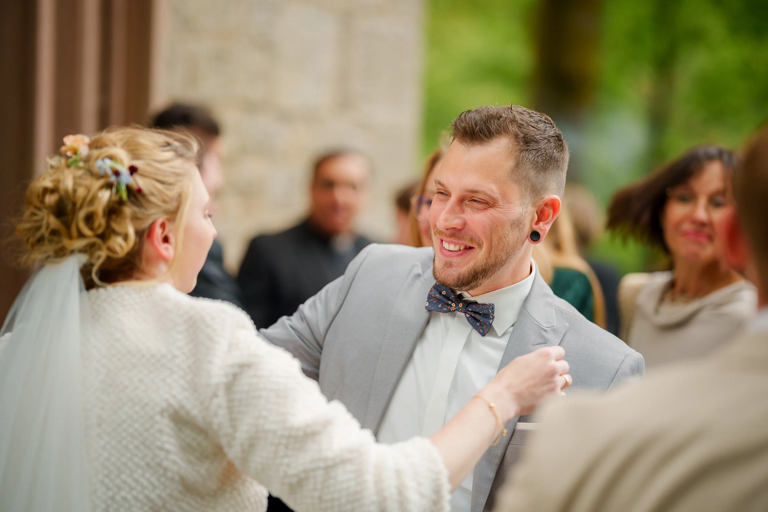 Ein Mann und eine Frau bei einer Hochzeit, fröhlich und lächelnd, im Gespräch, im Hintergrund andere Gäste.