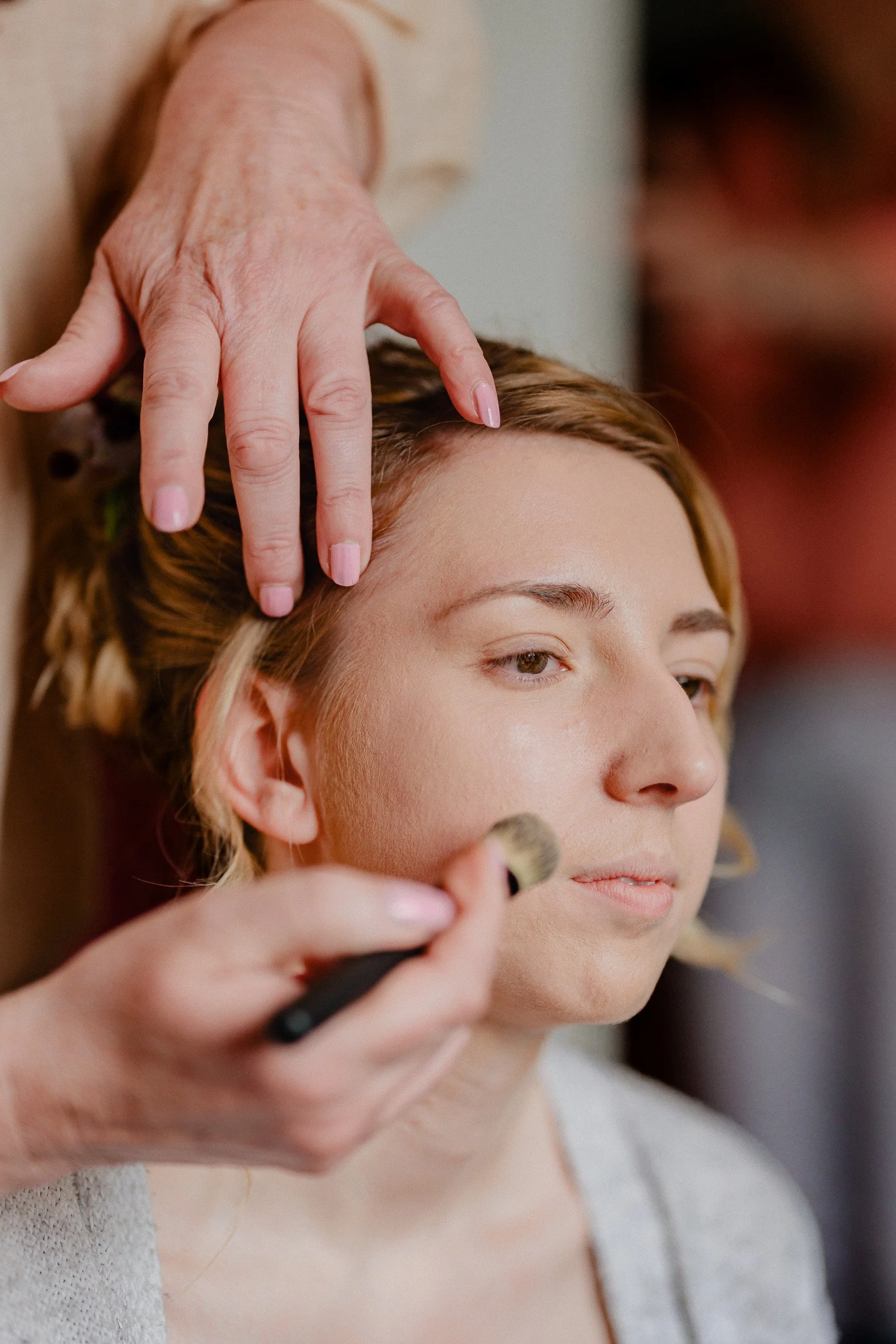 Getting Ready | Eine Frau wird für einen Makeup-Check im Gesicht geschminkt, während eine andere Person mit einem Pinsel arbeitet.