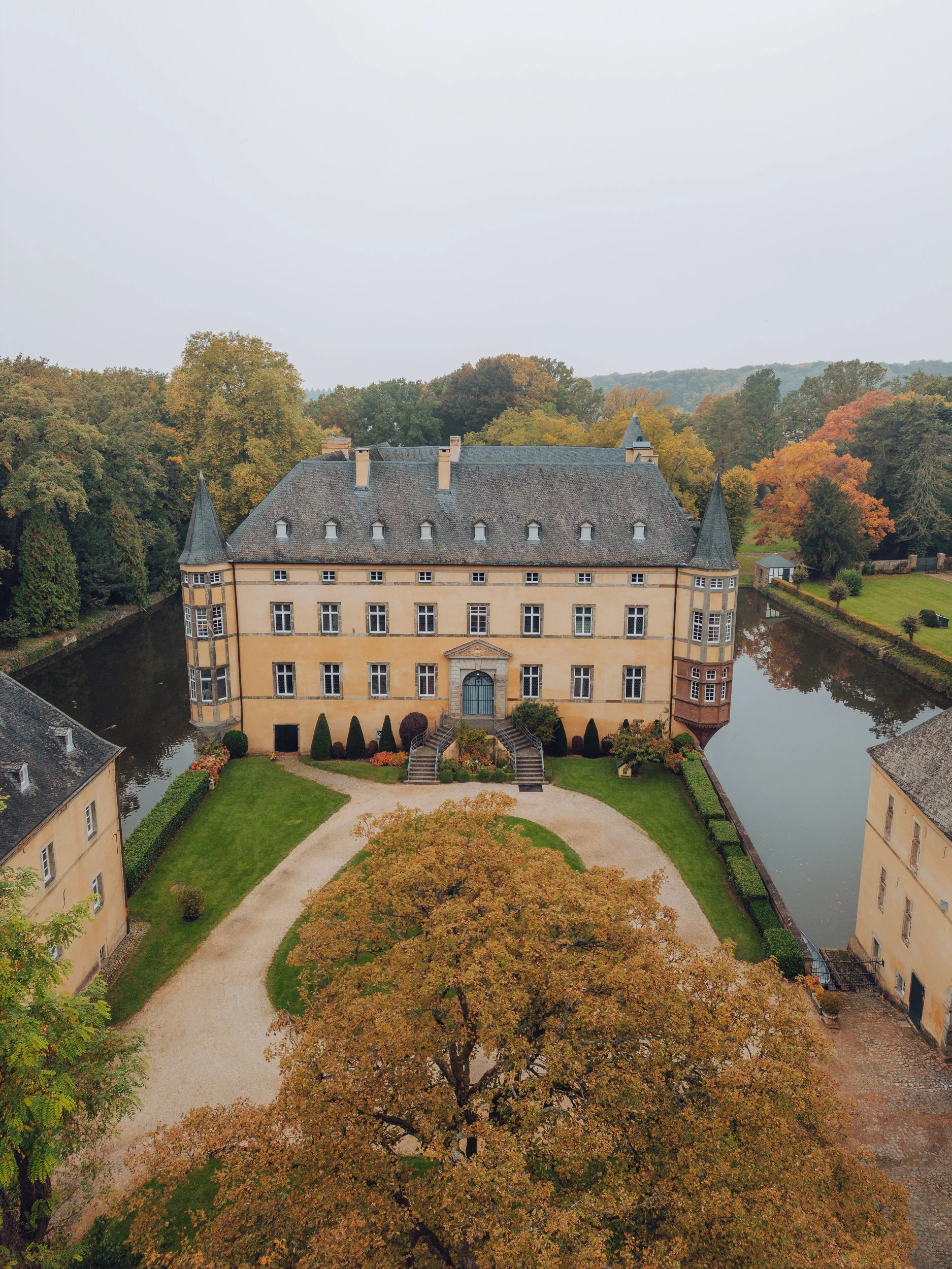 Blick auf ein Schloss im Herbst mit einem Wassergraben und bunten Bäumen im Park.