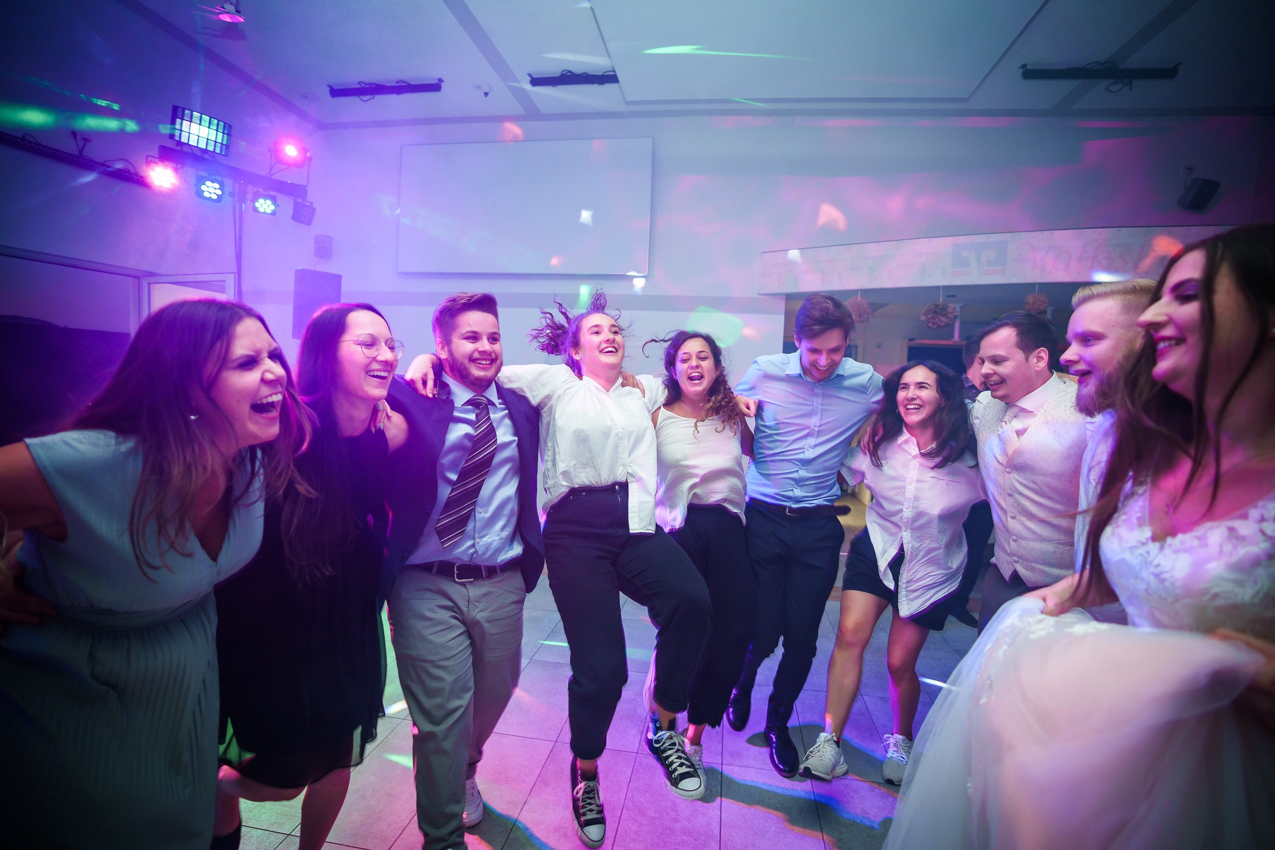 Gruppe von Menschen, die bei einer Party zusammen tanzen und lachen, umgeben von bunten Lichtern.