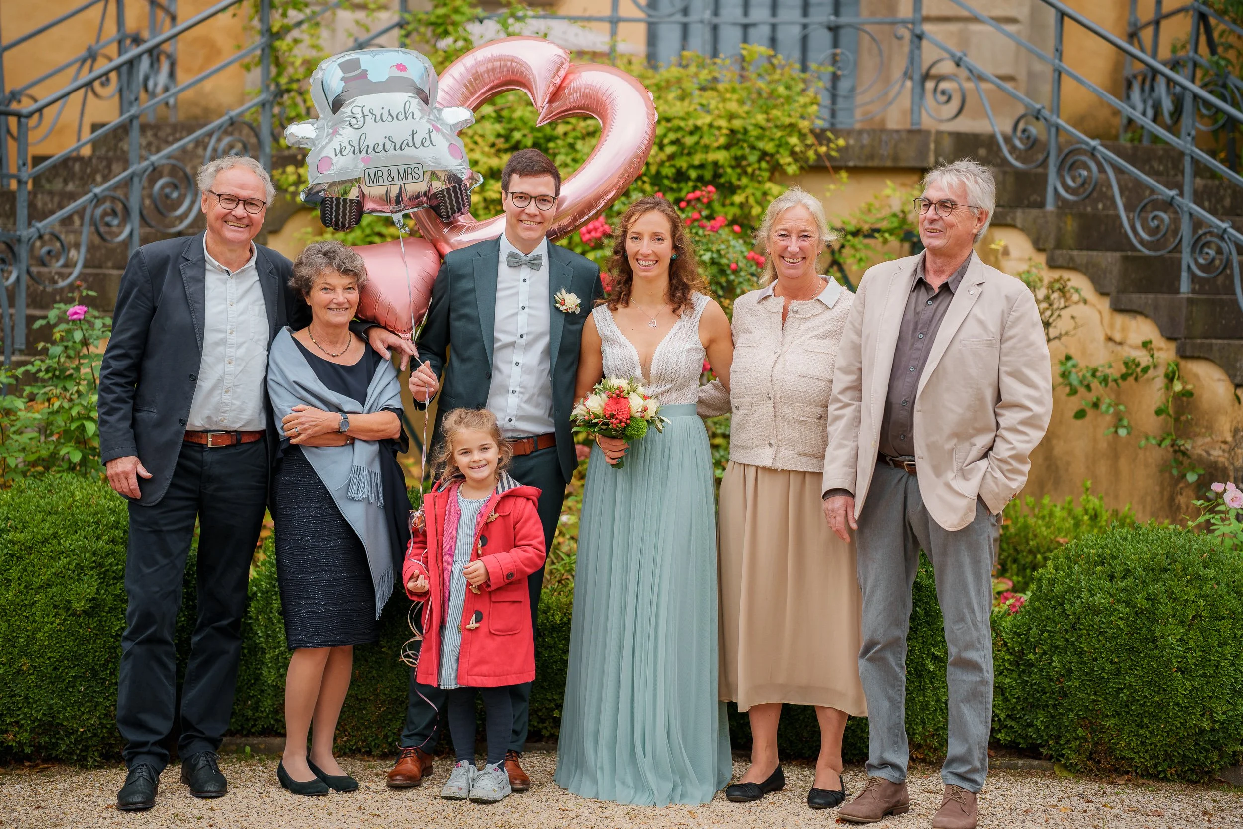 Gruppenfoto bei einer Hochzeit im Garten mit Braut, Bräutigam, Familienmitgliedern und Ballons. 