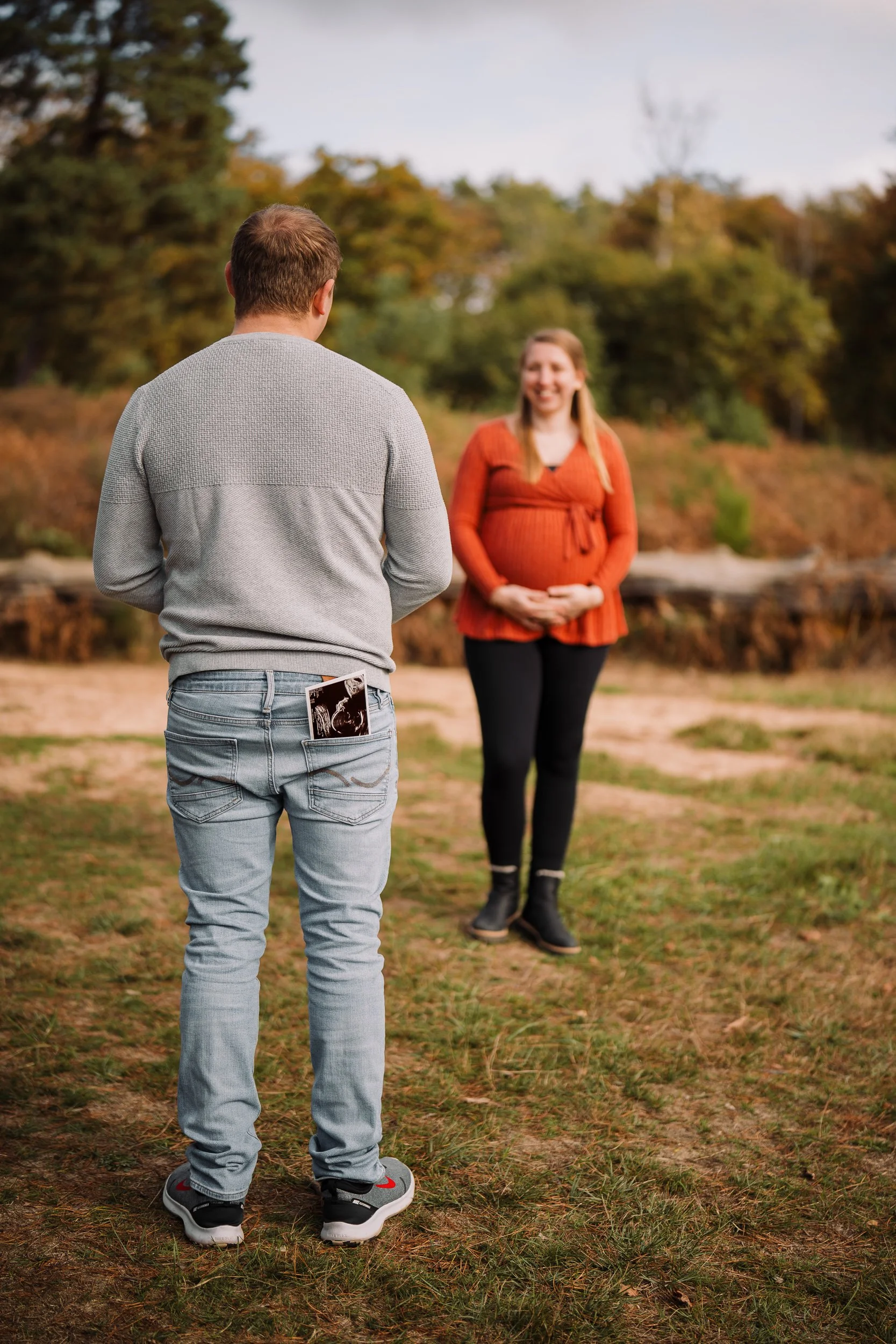Ein Mann schaut auf ein Ultraschallbild, während eine schwangere Frau ihm gegenübersitzt, im Freien bei Sonnenuntergang.
