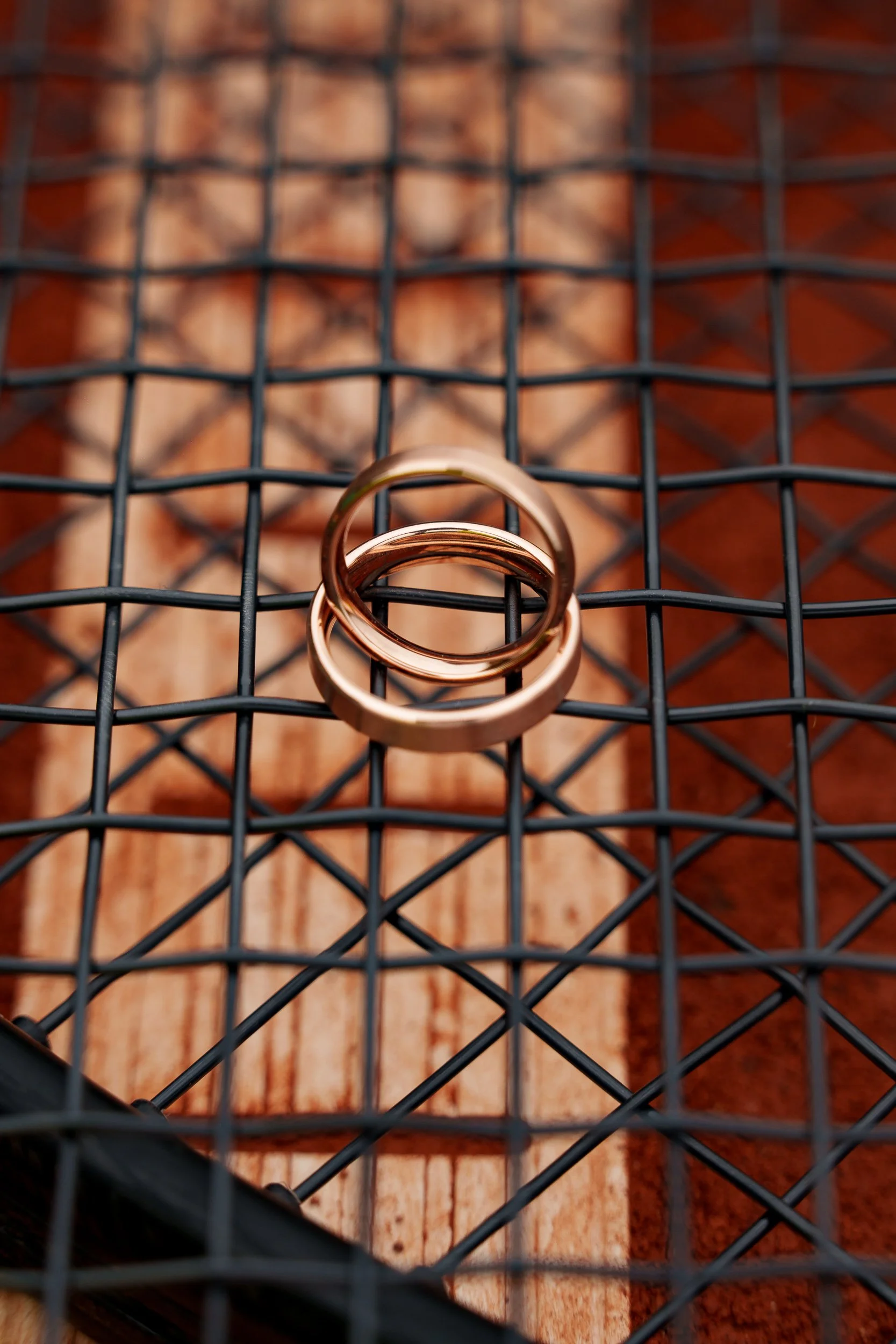 Zwei goldene Ringe auf einem schwarzen Gitter, im Hintergrund eine Holzfläche mit eingekerbter Struktur.