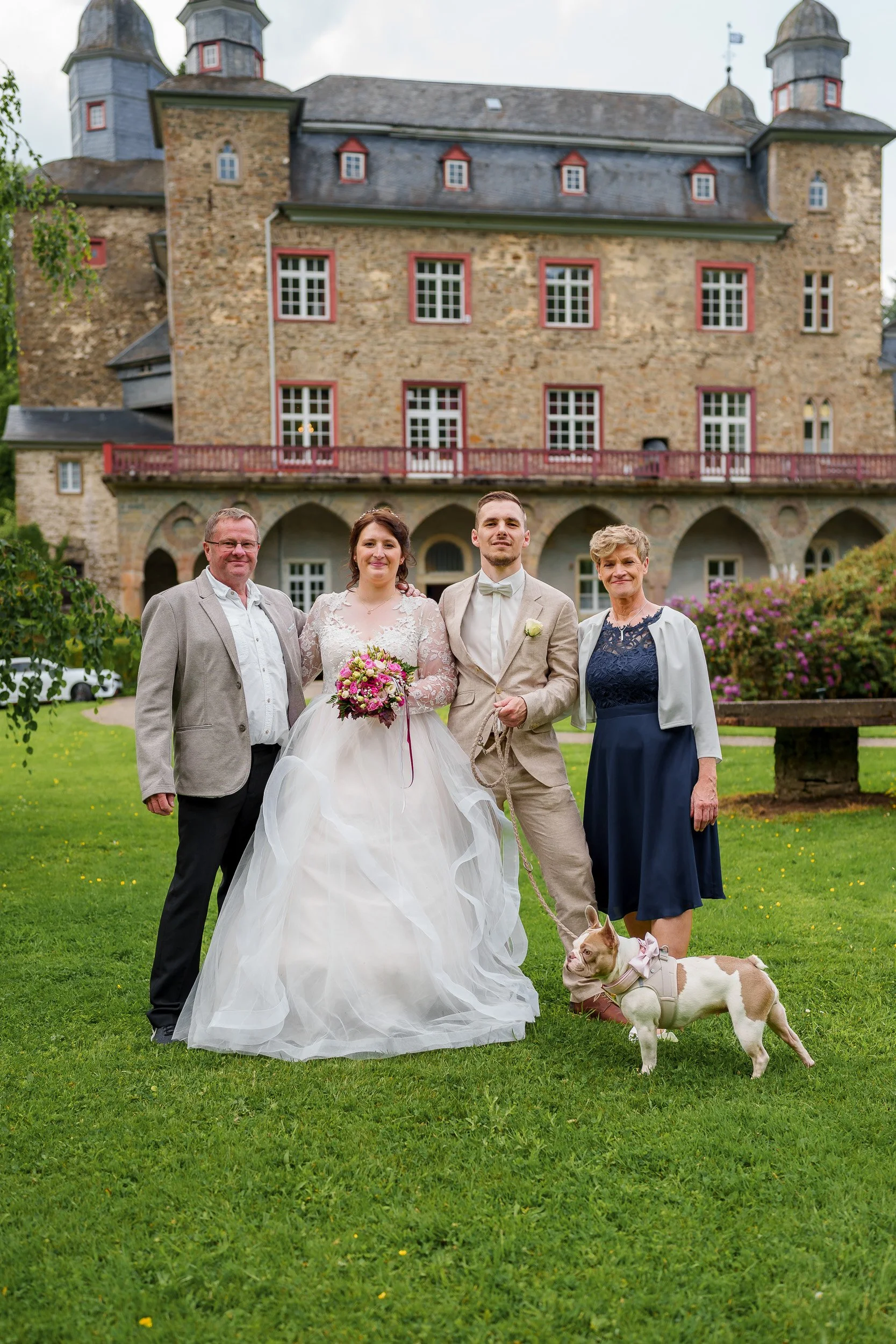 Hochzeitspaar mit Familie und Hund vor einem Schloss