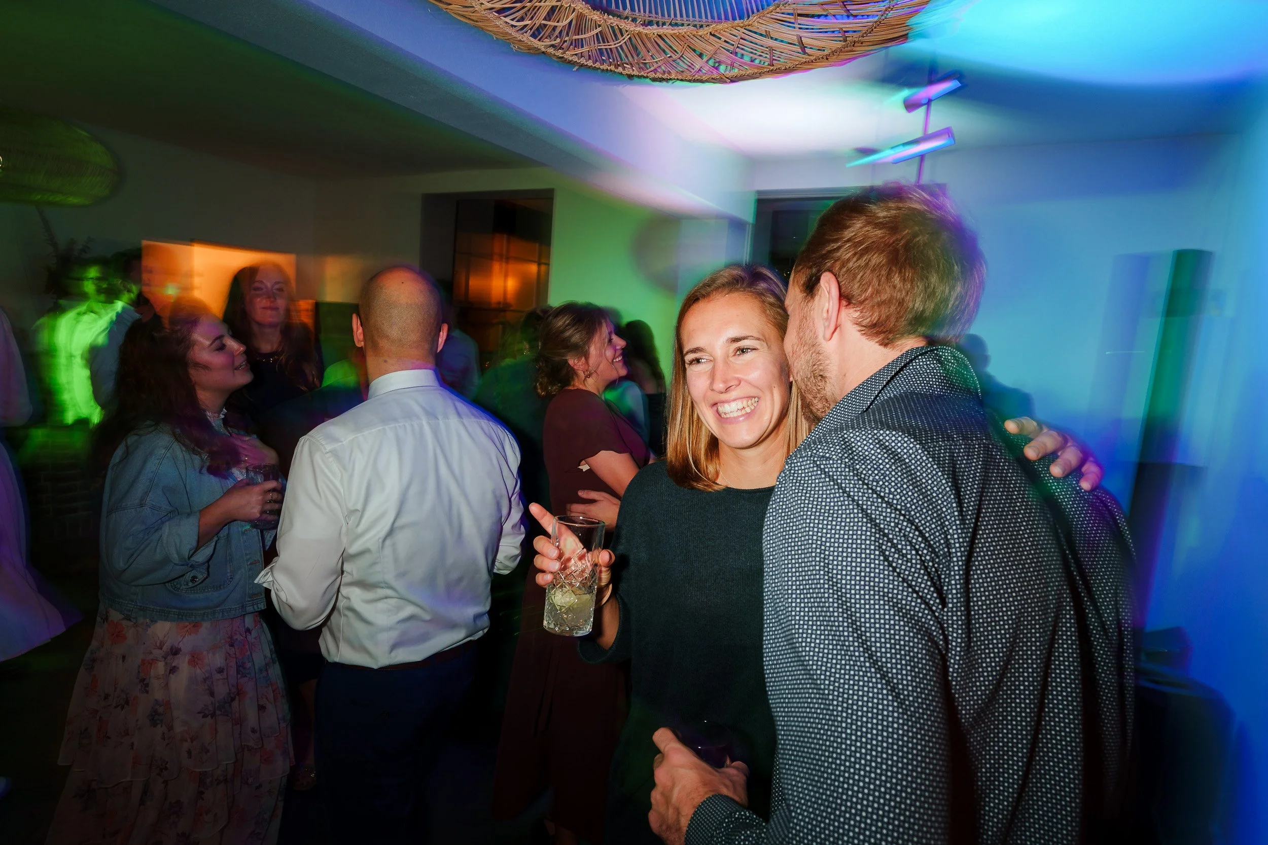 Menschen feiern und tanzen auf einer Party in einem Raum mit bunten Lichtern.