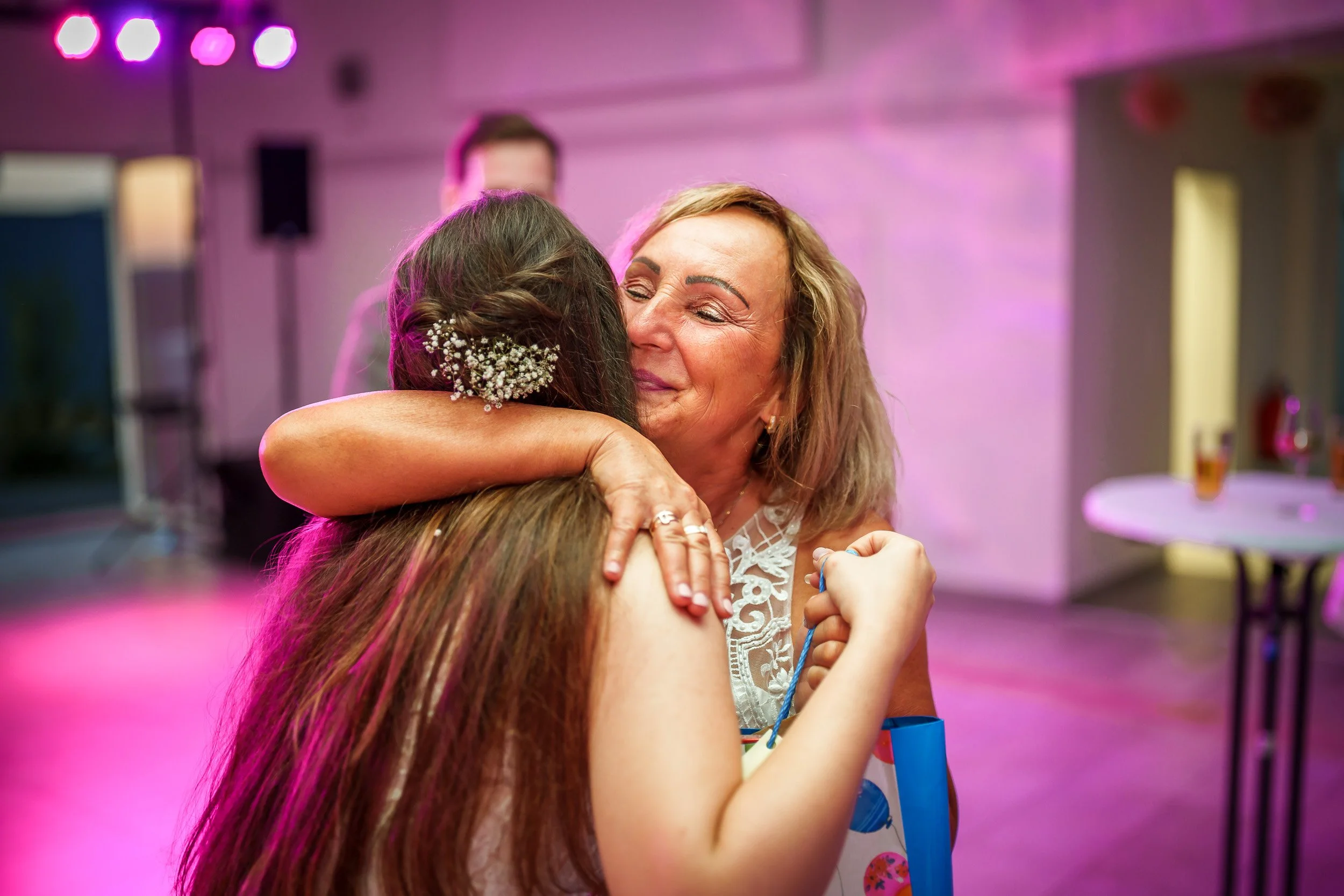 Zwei Frauen umarmen sich herzlich bei einer Feier, im Hintergrund bunte Beleuchtung.
